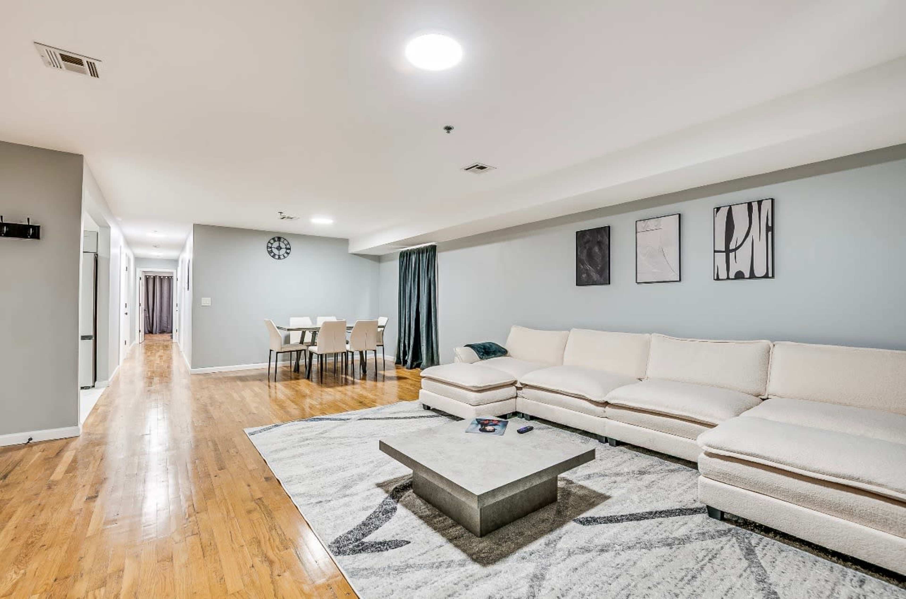 The image shows a spacious living room with a white sectional sofa, a gray rug, and a dining area in the background.
