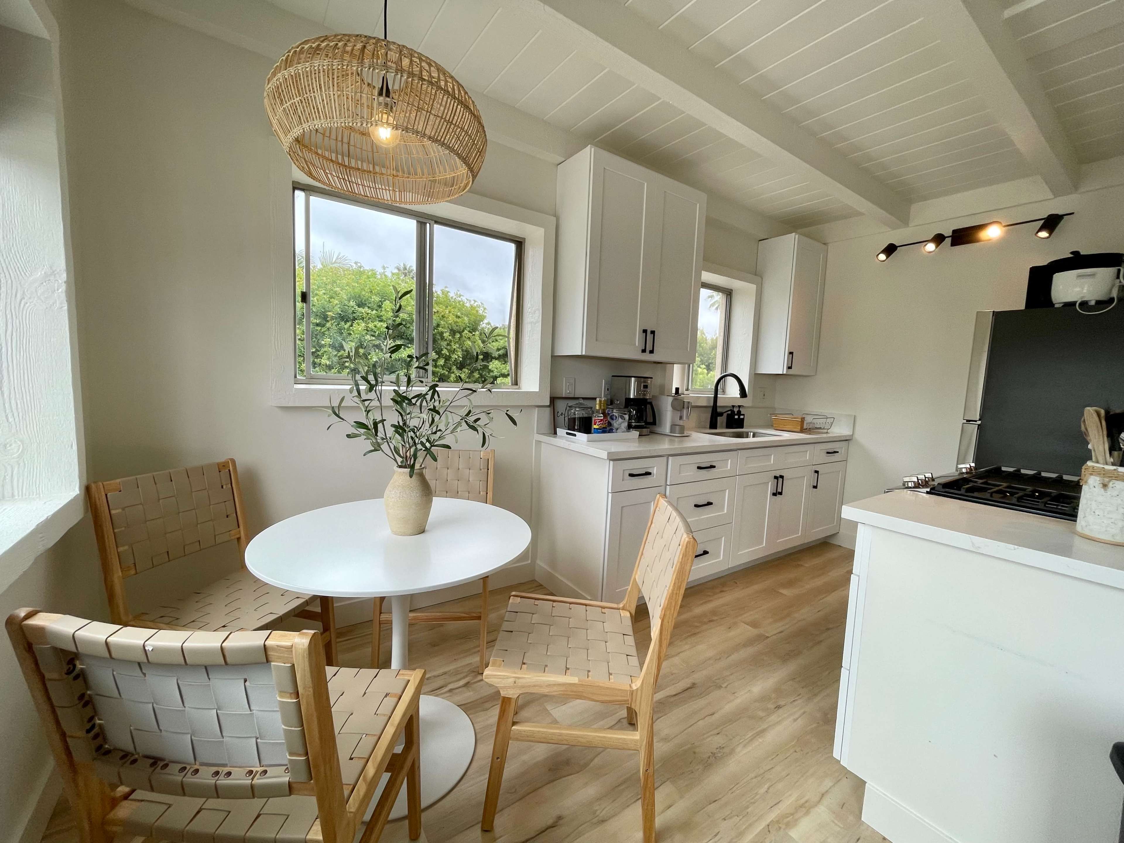 A cozy kitchen with a round dining table surrounded by two wooden chairs and two woven chairs, featuring white cabinets and a black stove.