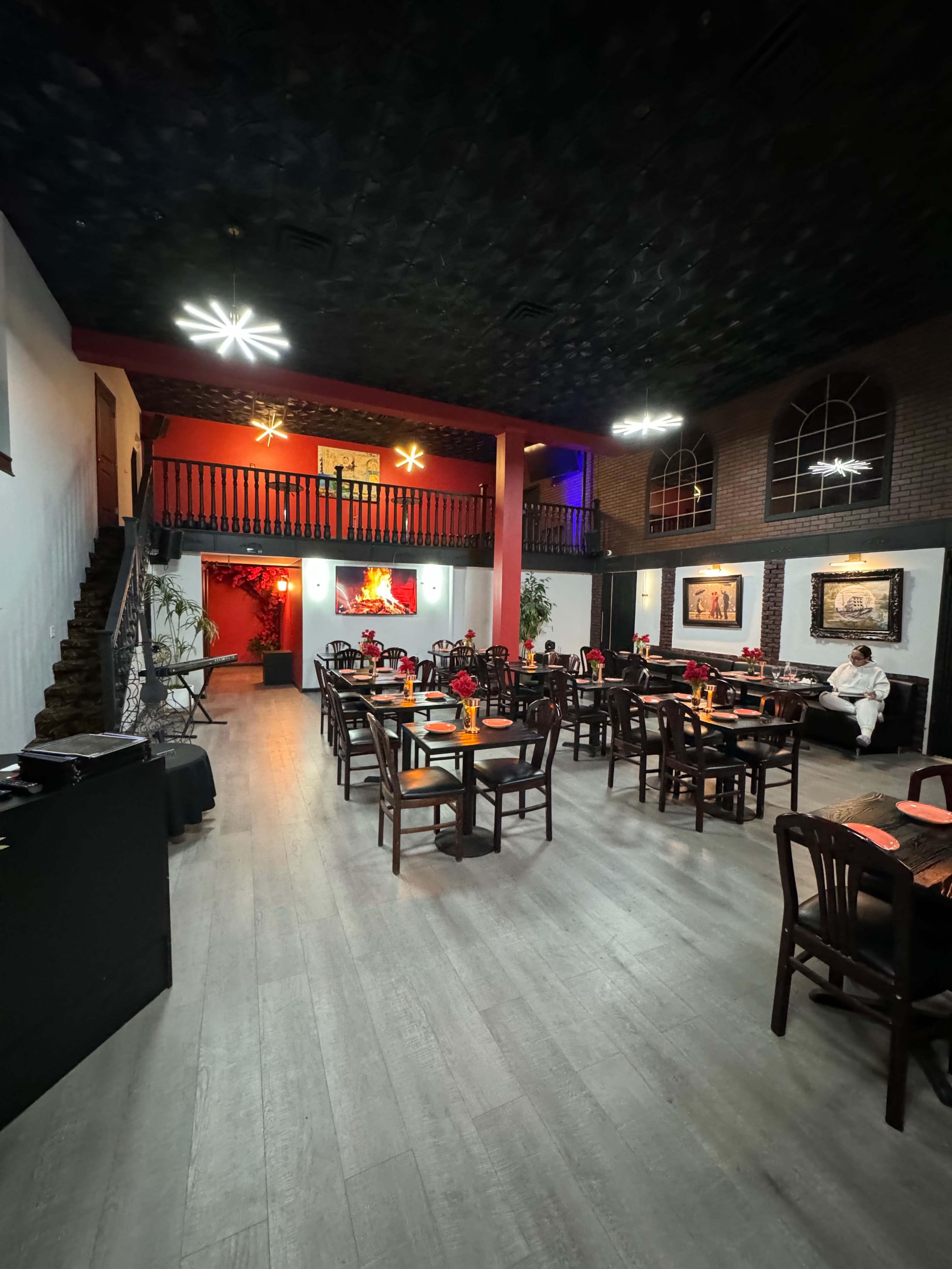 A spacious restaurant with several wooden tables set for dining, a staircase in the background, and decorative lighting fixtures on the ceiling.