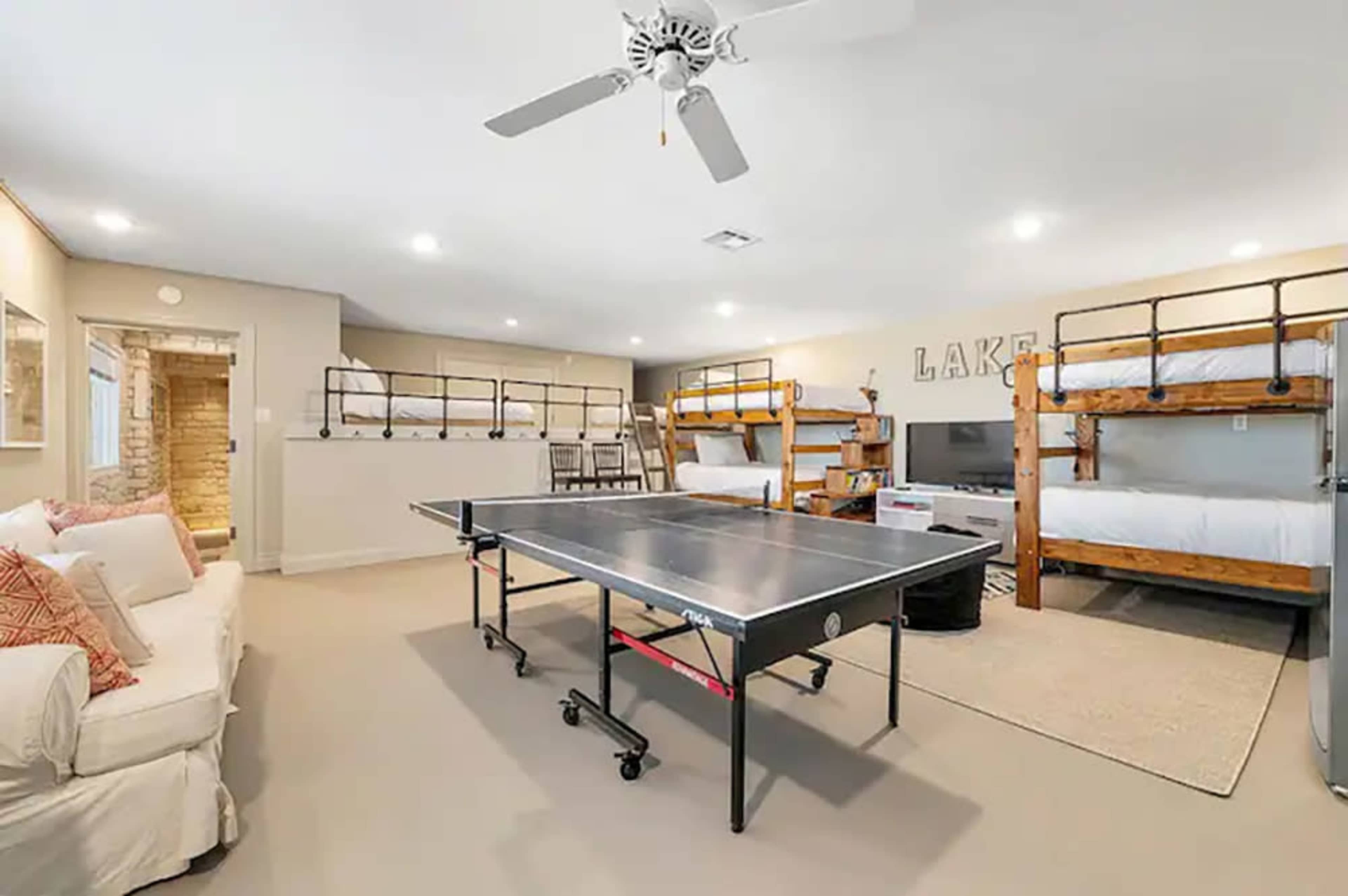 A spacious room with bunk beds, a ping pong table in the center, and a seating area with a couch.