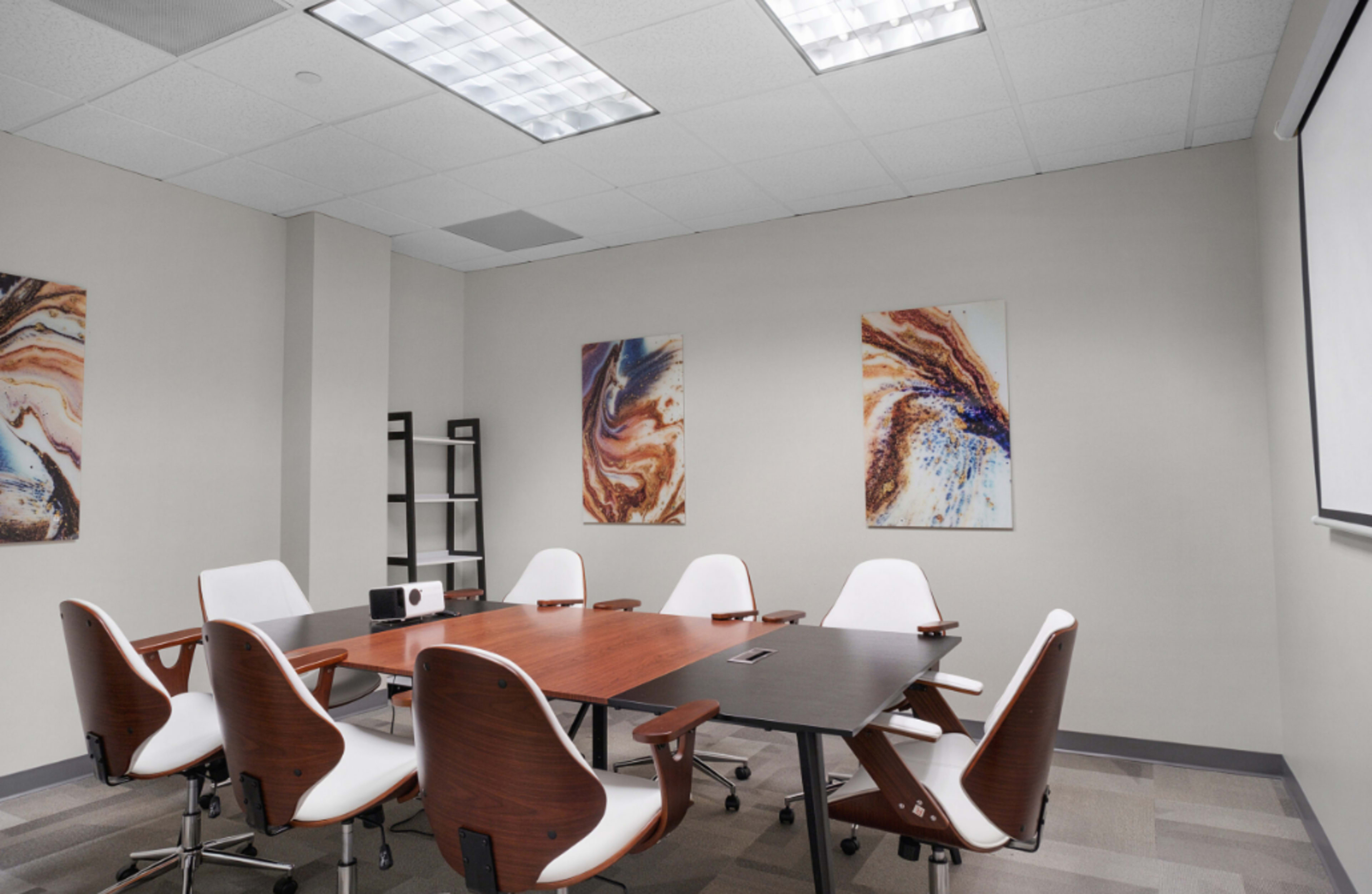 A conference room with a large wooden table surrounded by white chairs and artwork on the walls.