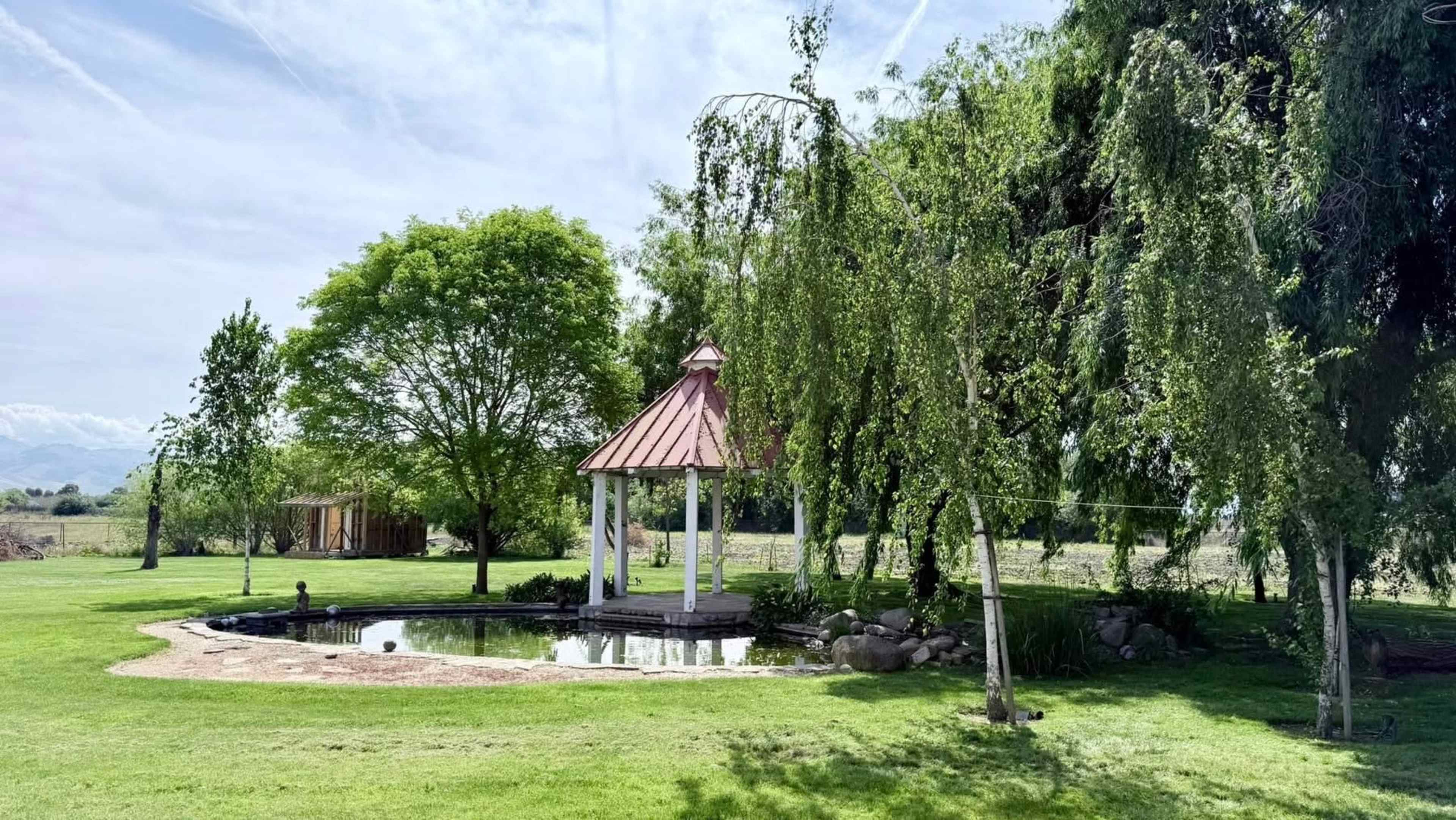 The image shows a landscaped area with a pond and a gazebo surrounded by trees and grass.