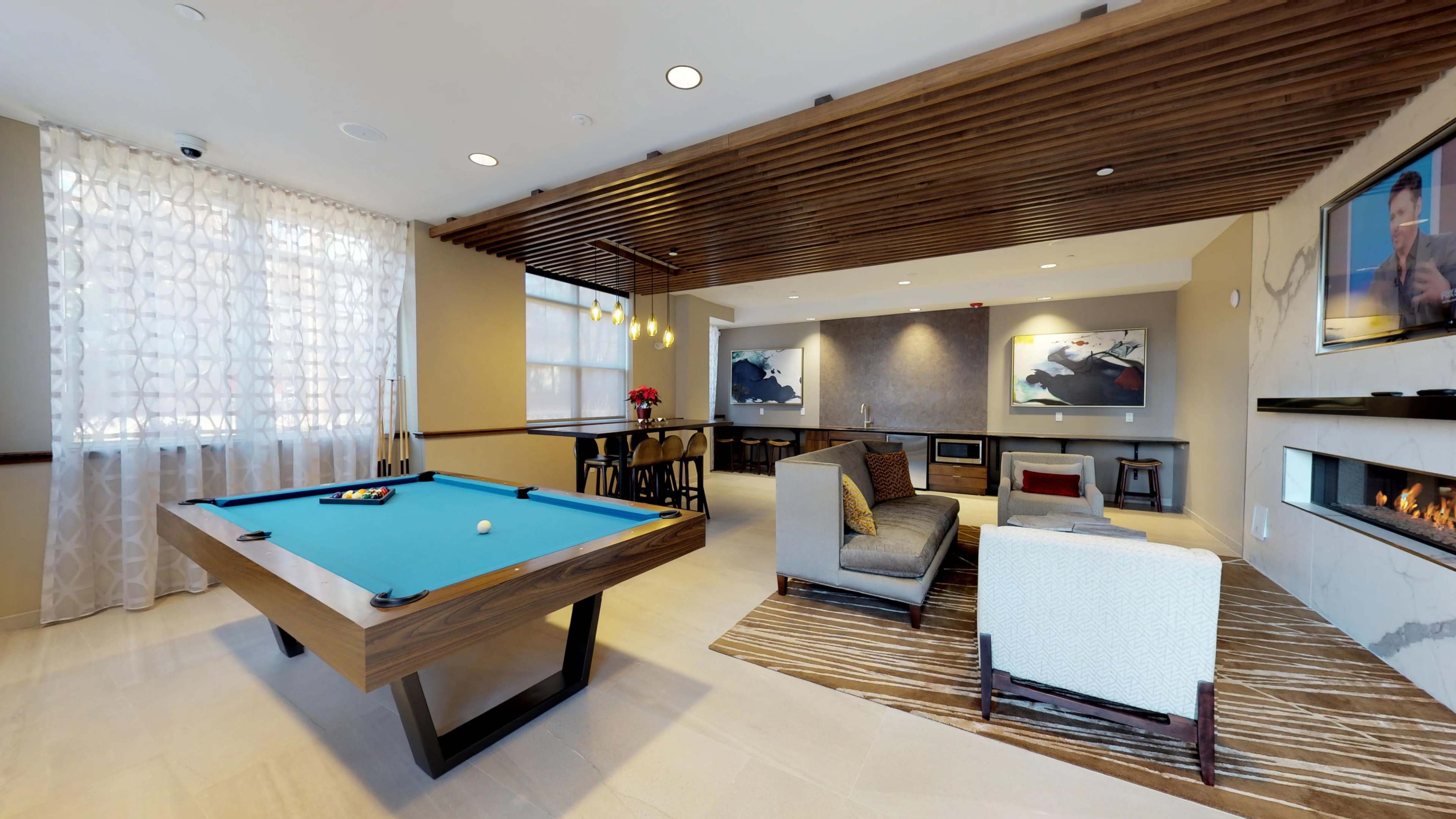 The image shows a spacious room featuring a pool table, a seating area with a couch, and a fireplace, along with a dining area in the background.