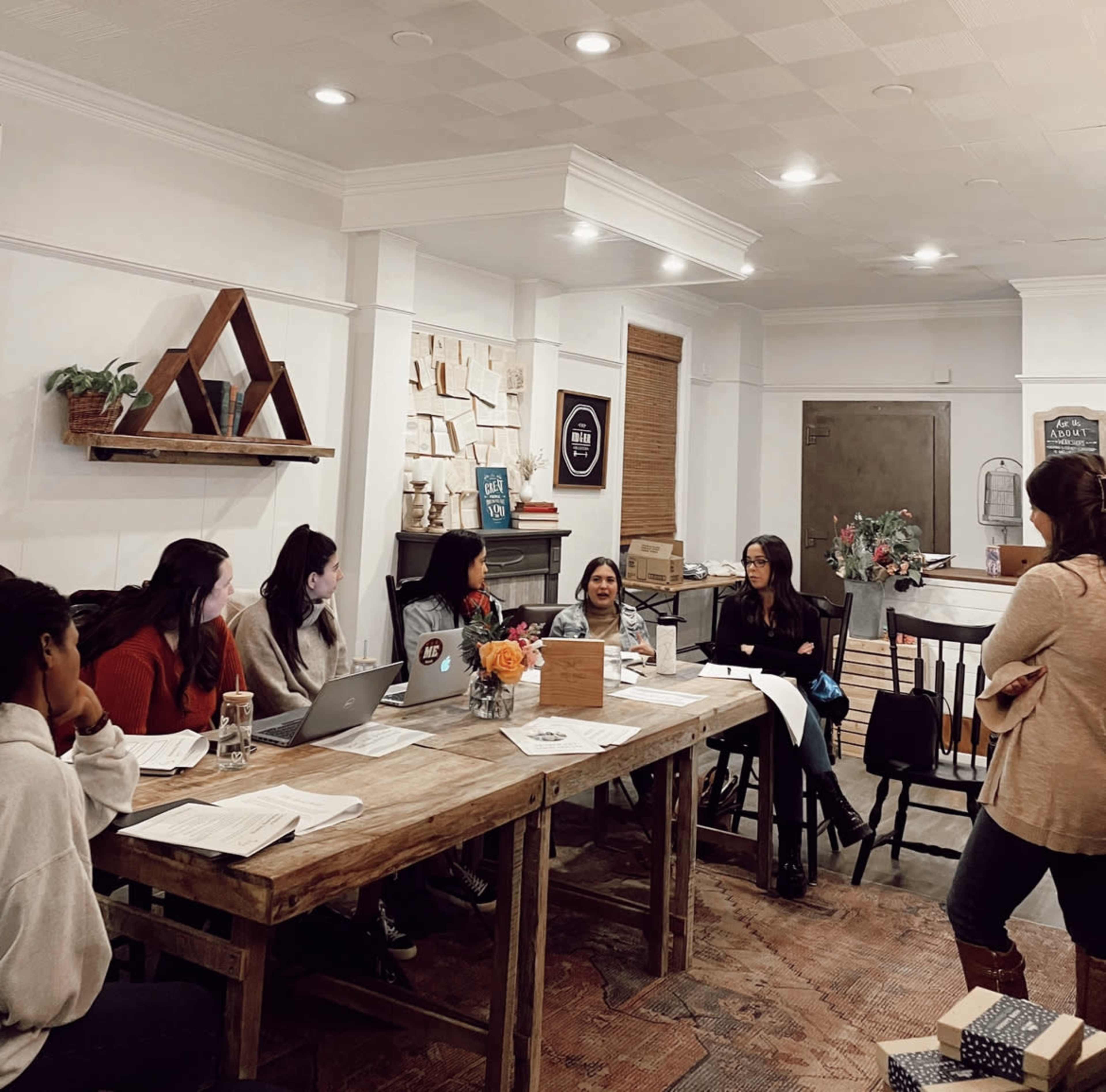 A group of six individuals engage in discussion around a large wooden table in a stylish meeting room.