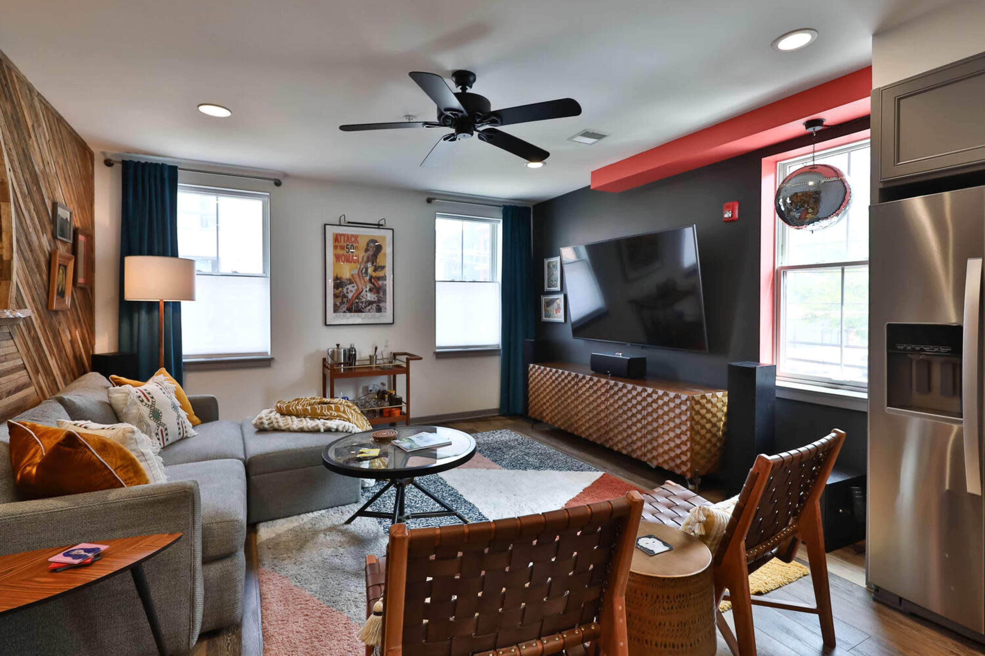 A modern living room with a gray sectional sofa, a large wall-mounted TV, and a combination of colorful decor and furniture.