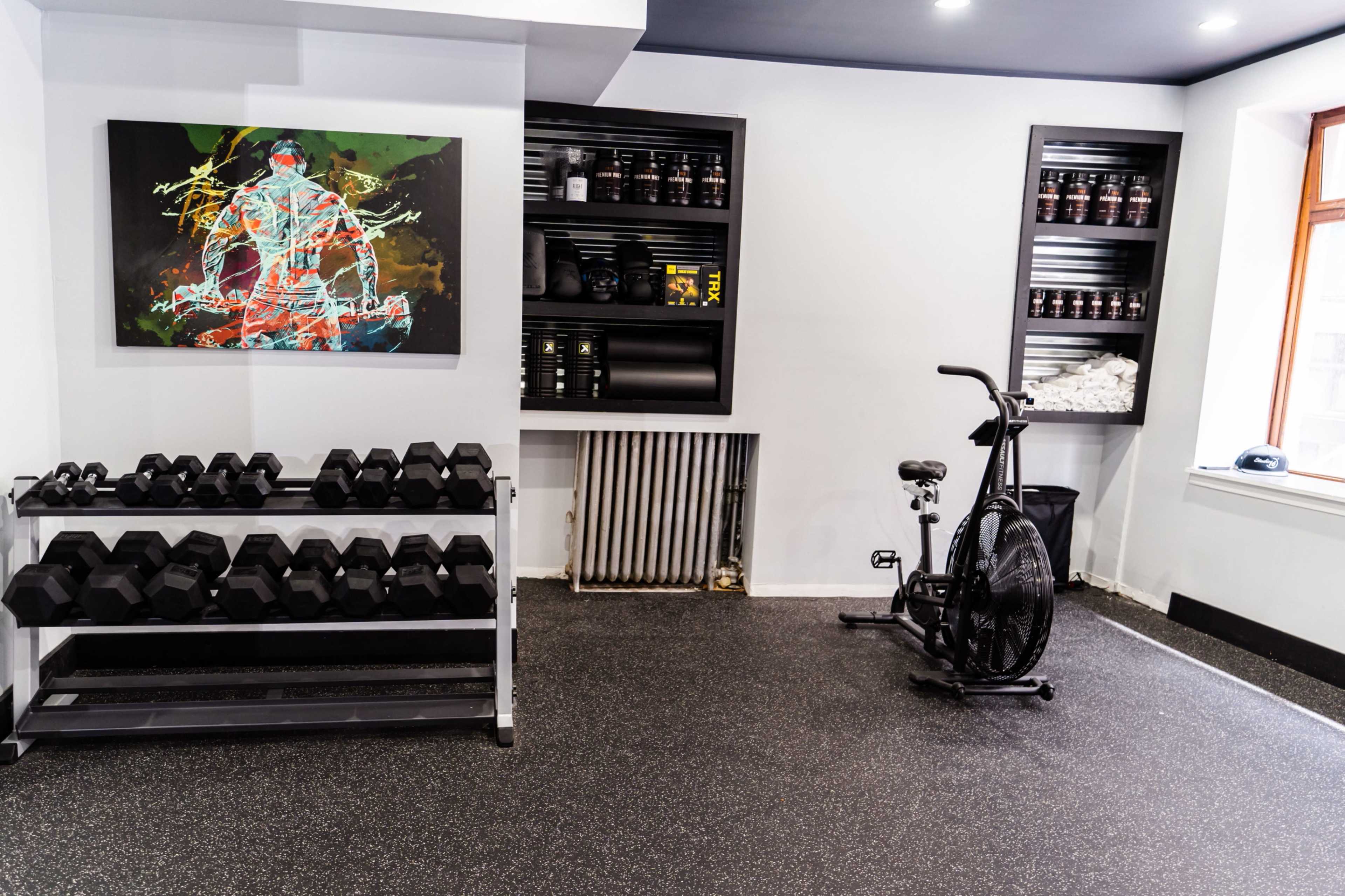 A home gym featuring a rack of dumbbells and an exercise bike against a wall adorned with a colorful abstract painting.