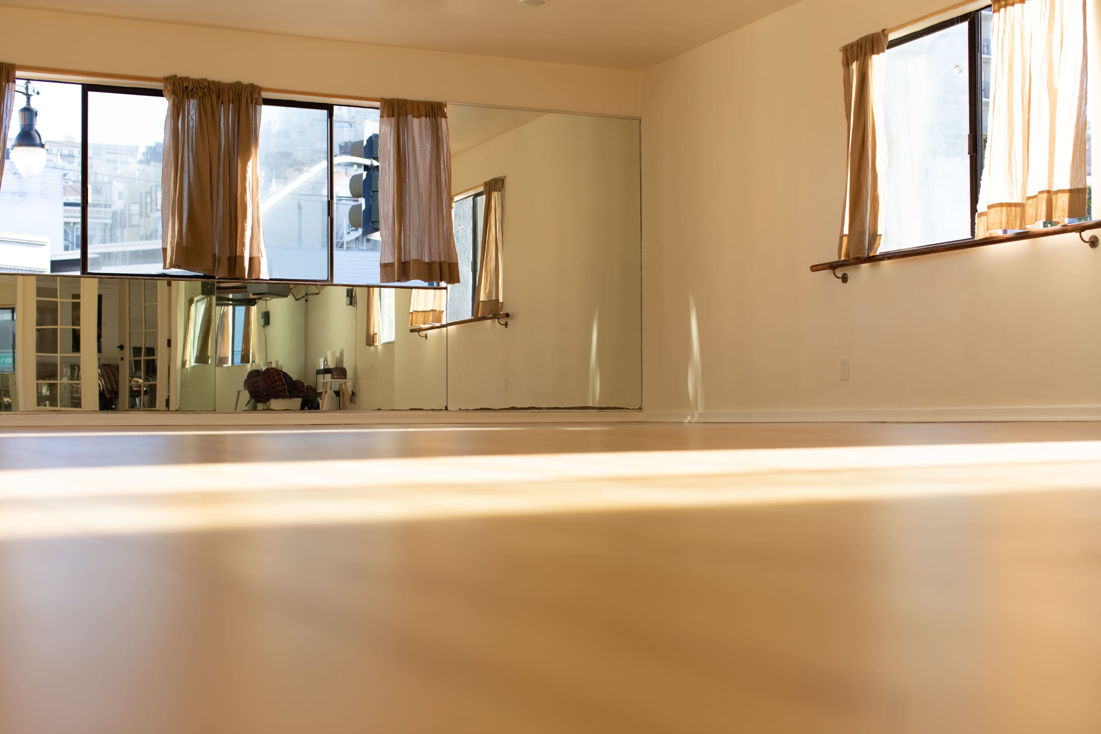 A bright, empty room with large windows and a floor-to-ceiling mirror.