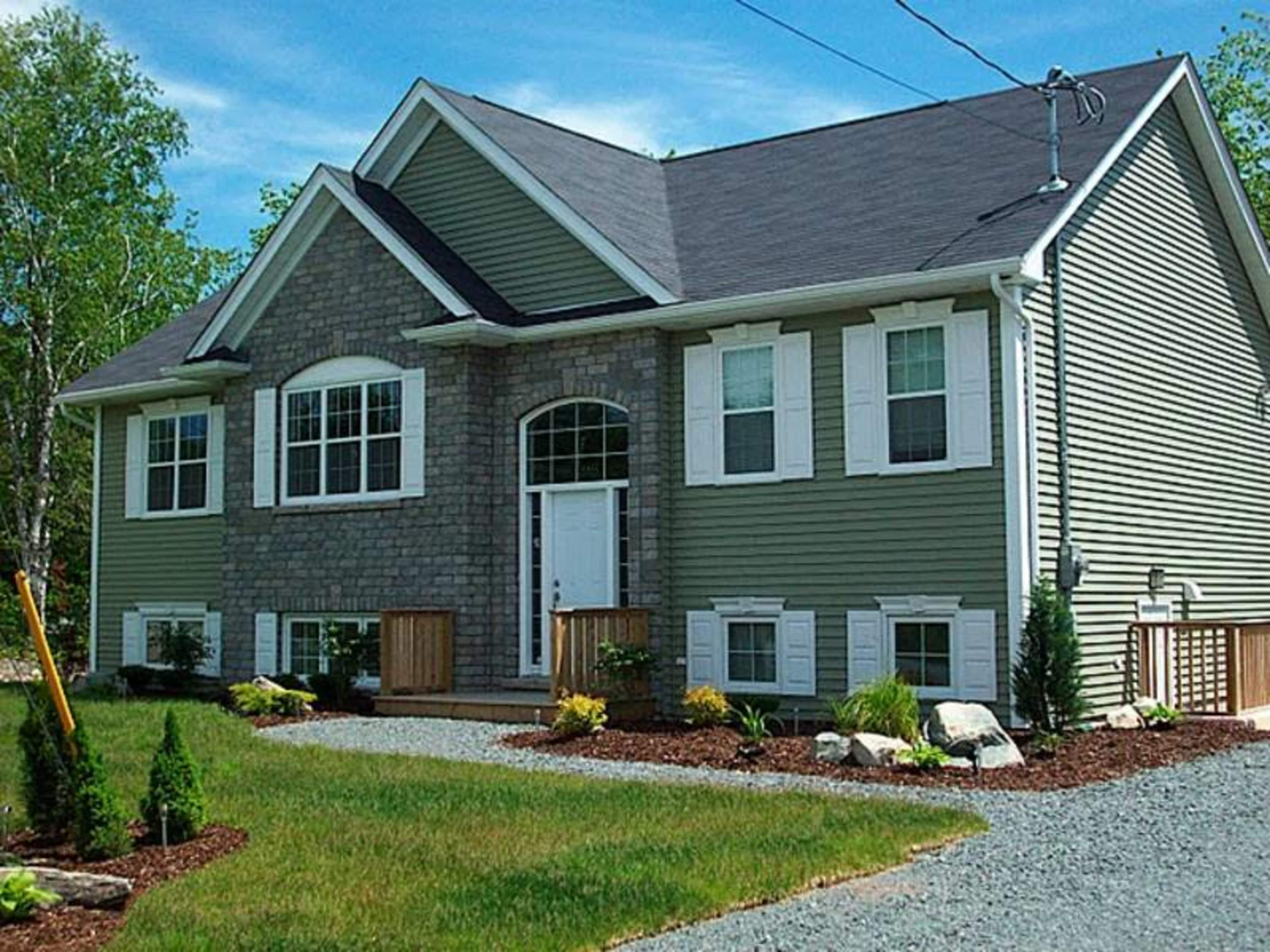 A two-story house features a stone front, gray siding, and a landscaped yard with shrubs and rocks.