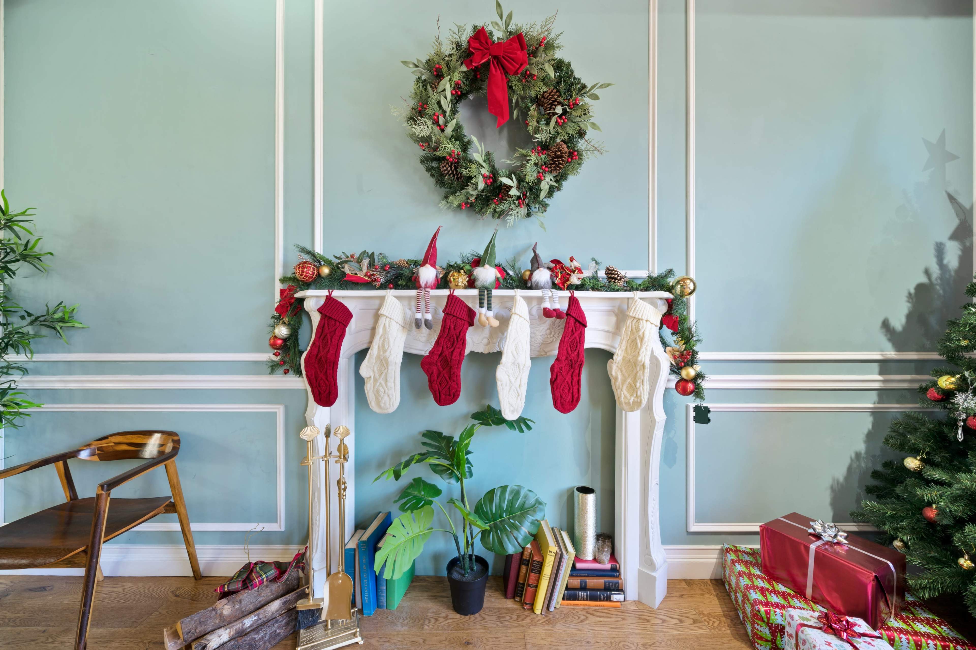 A decorated mantelpiece features stockings, a wreath, and festive decor, with a green wall and a nearby Christmas tree.