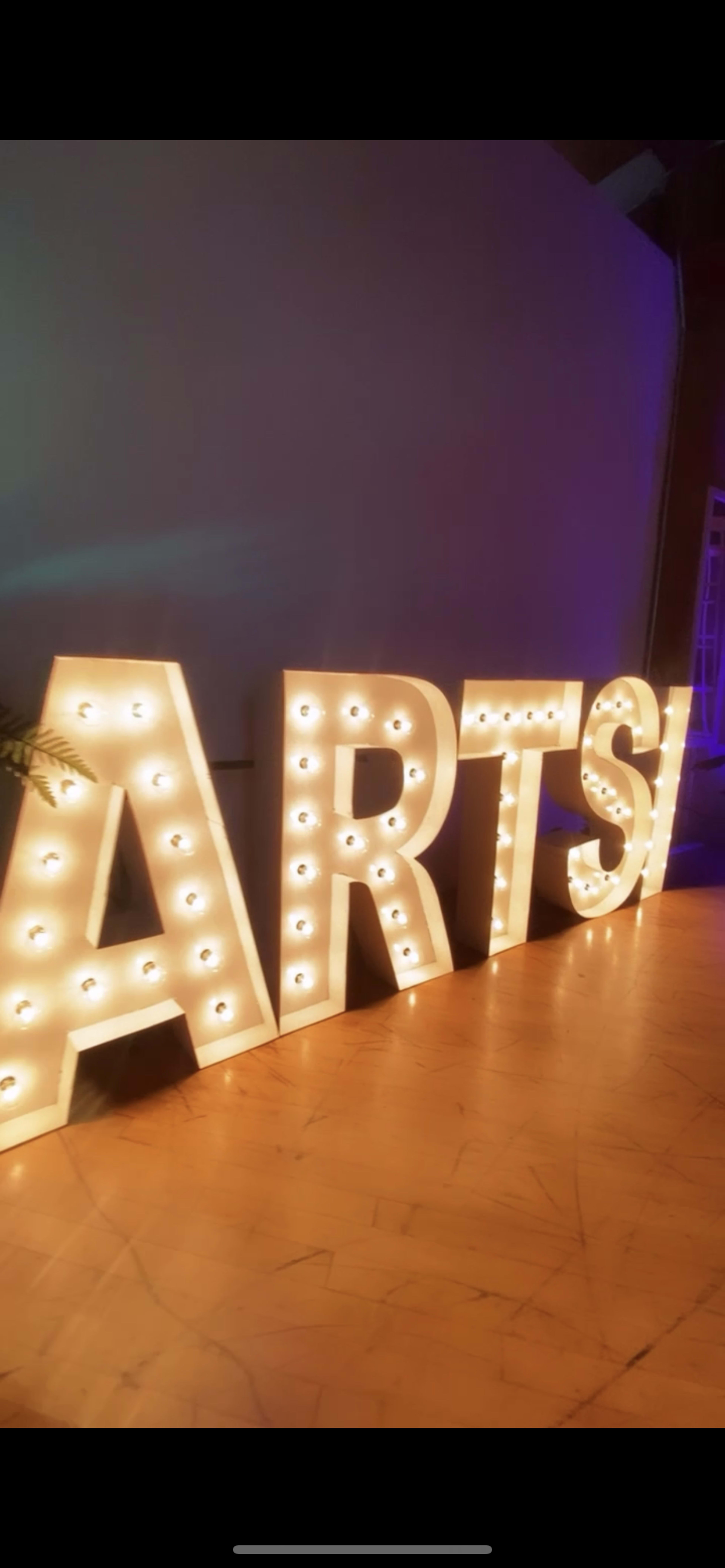 Large illuminated letters spelling "ARTS" set against a wall.
