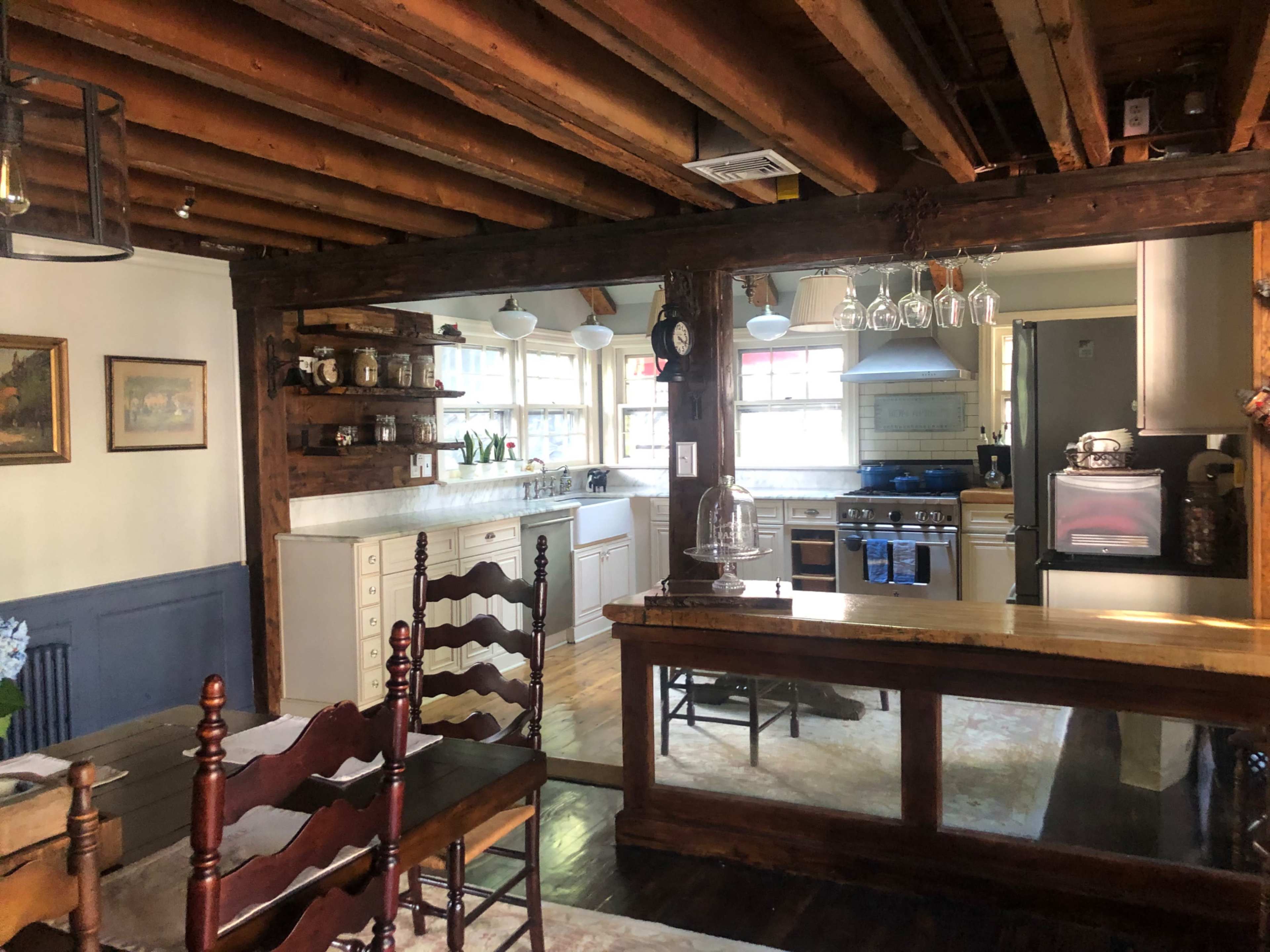 A rustic kitchen with wooden beams, a central dining table, and an open layout featuring modern appliances.