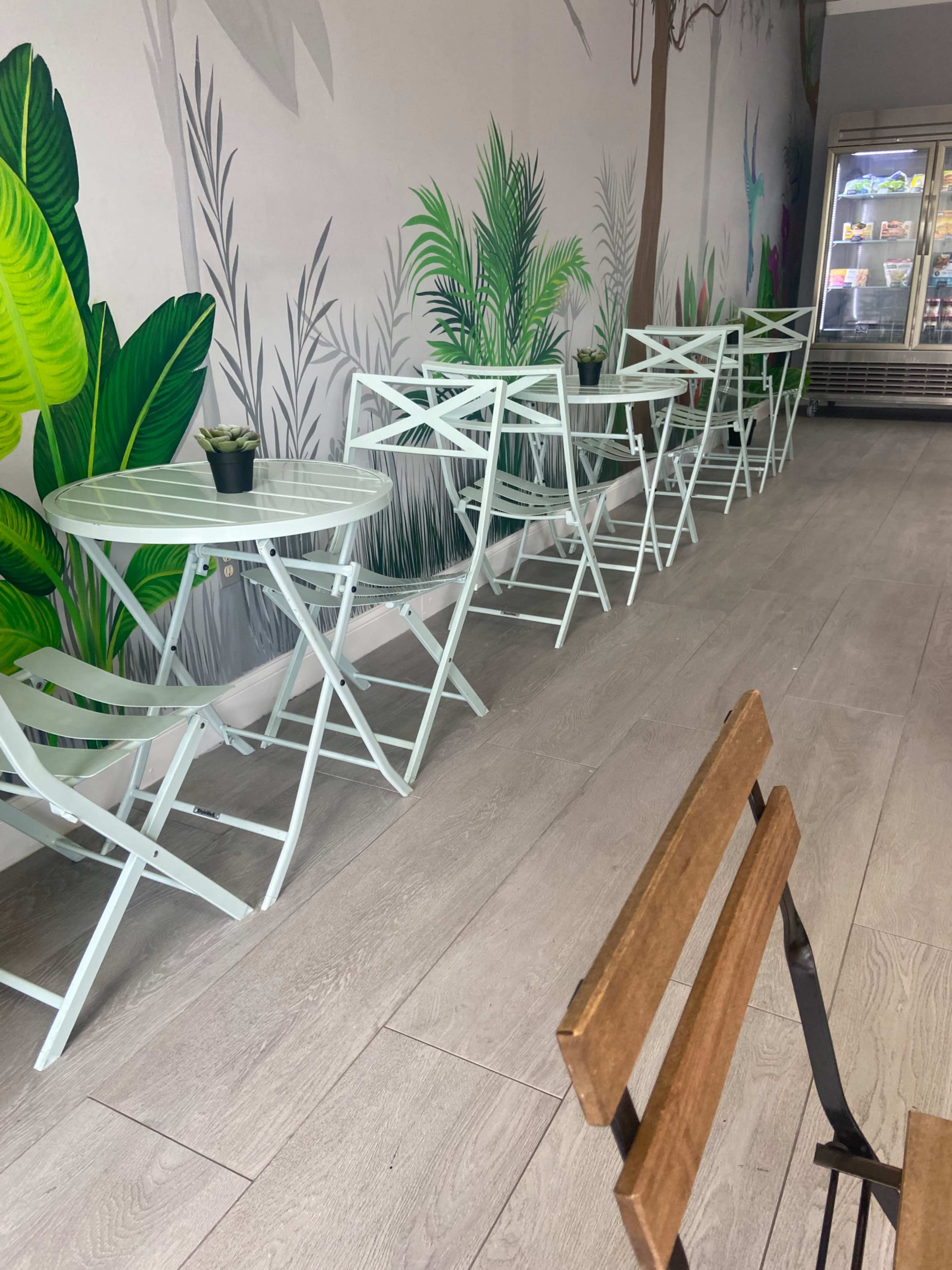 A row of light green, folding tables and chairs situated along a wall adorned with tropical plant murals in a cafe setting.