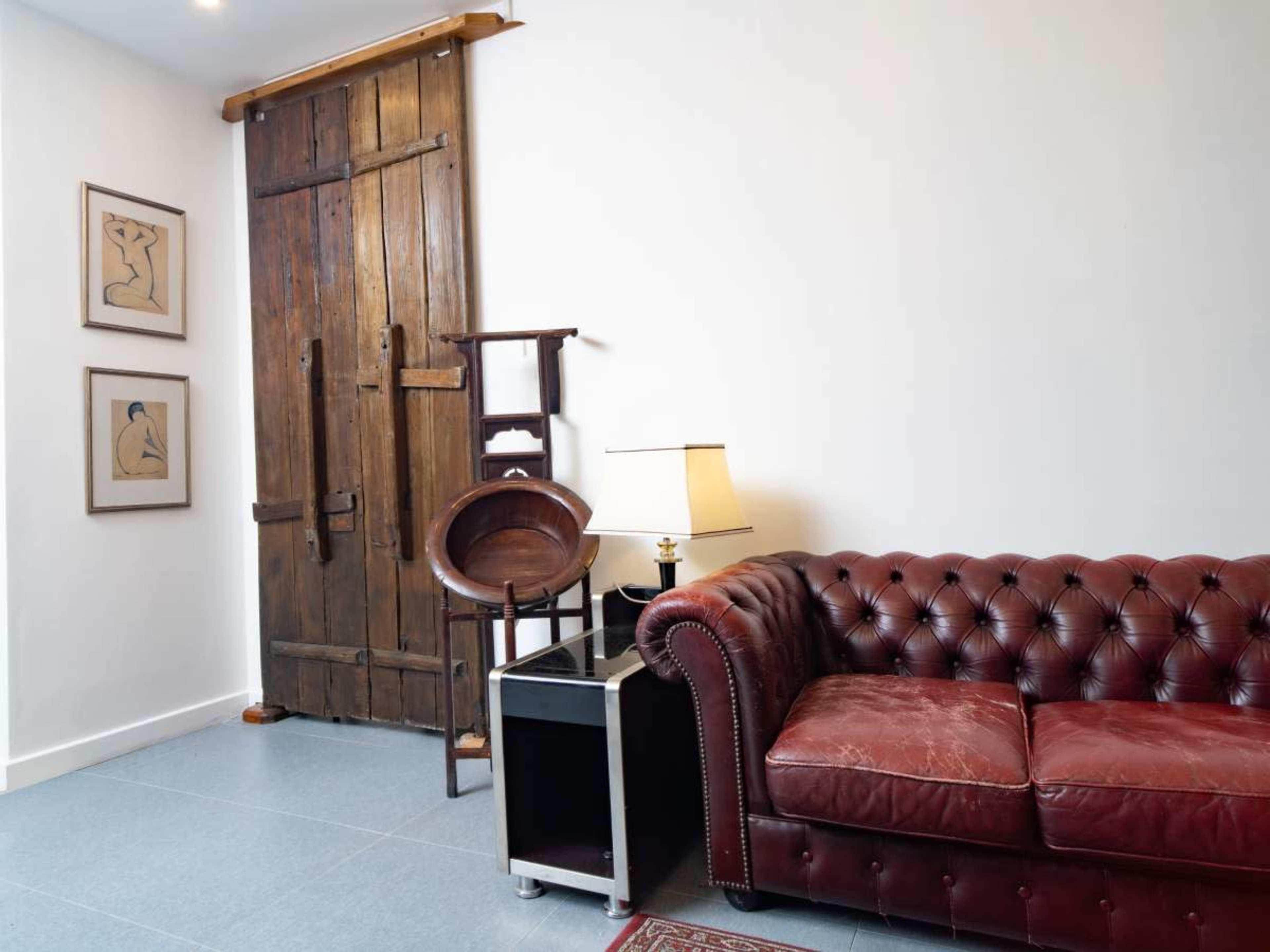 The image shows a living room with a red leather Chesterfield sofa, a wooden door, and framed artwork on the walls.