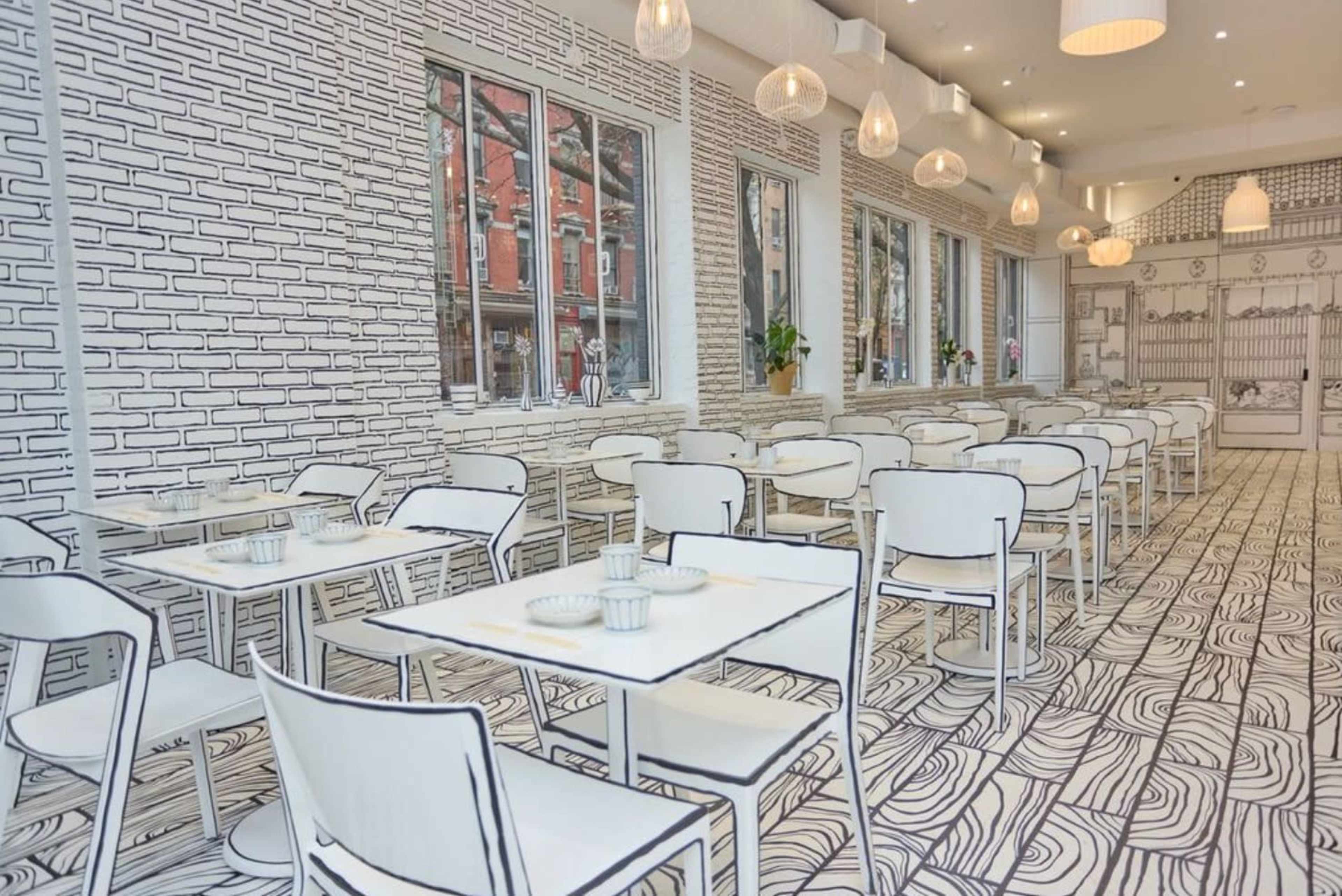 The image shows a restaurant with a minimalist design featuring tables and chairs, all in white, against a backdrop of hand-drawn brick and wood patterns on the walls and floor.