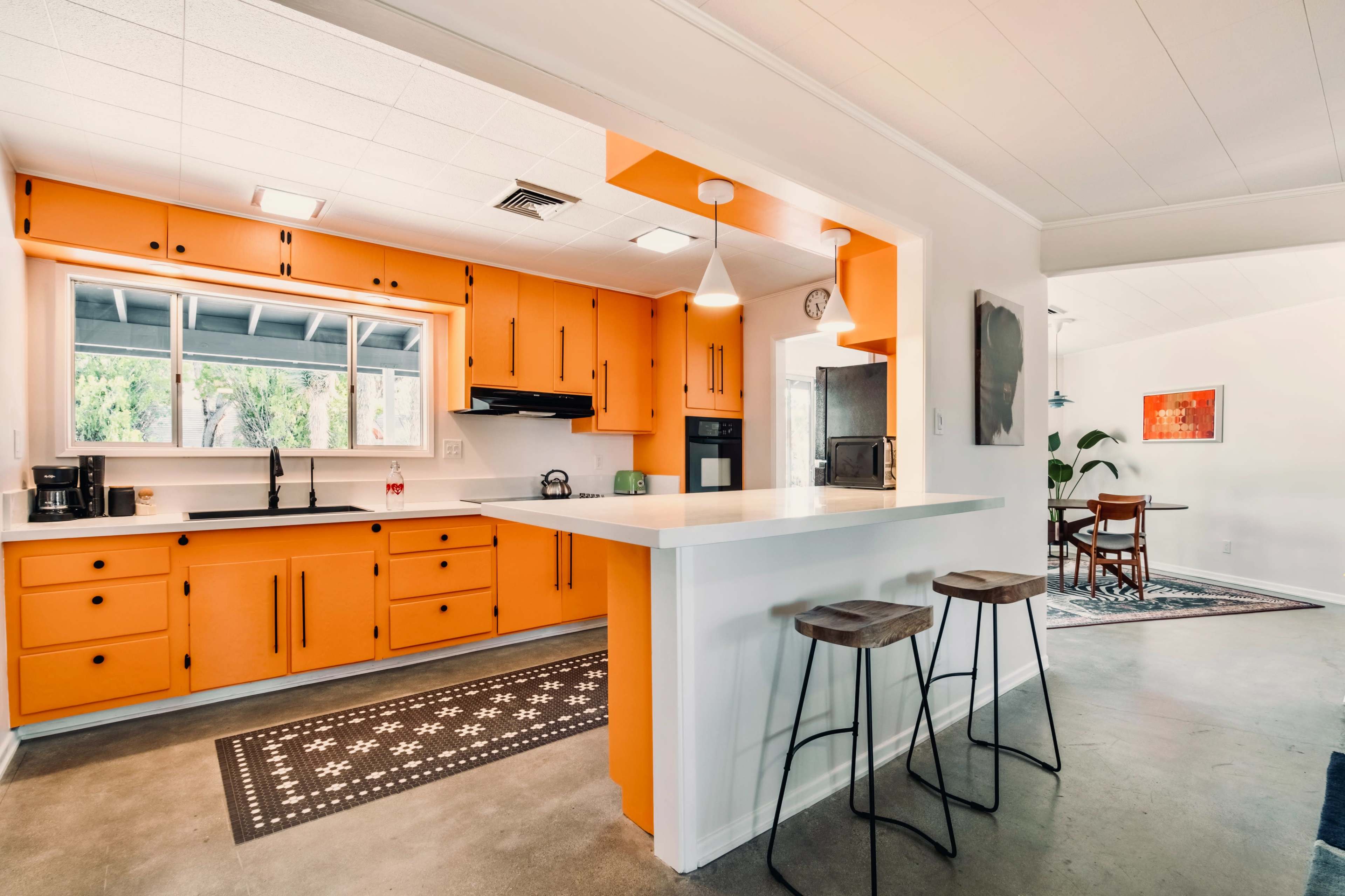 The kitchen features orange cabinets, a central island with bar stools, and a view of a dining area with a table and chairs.