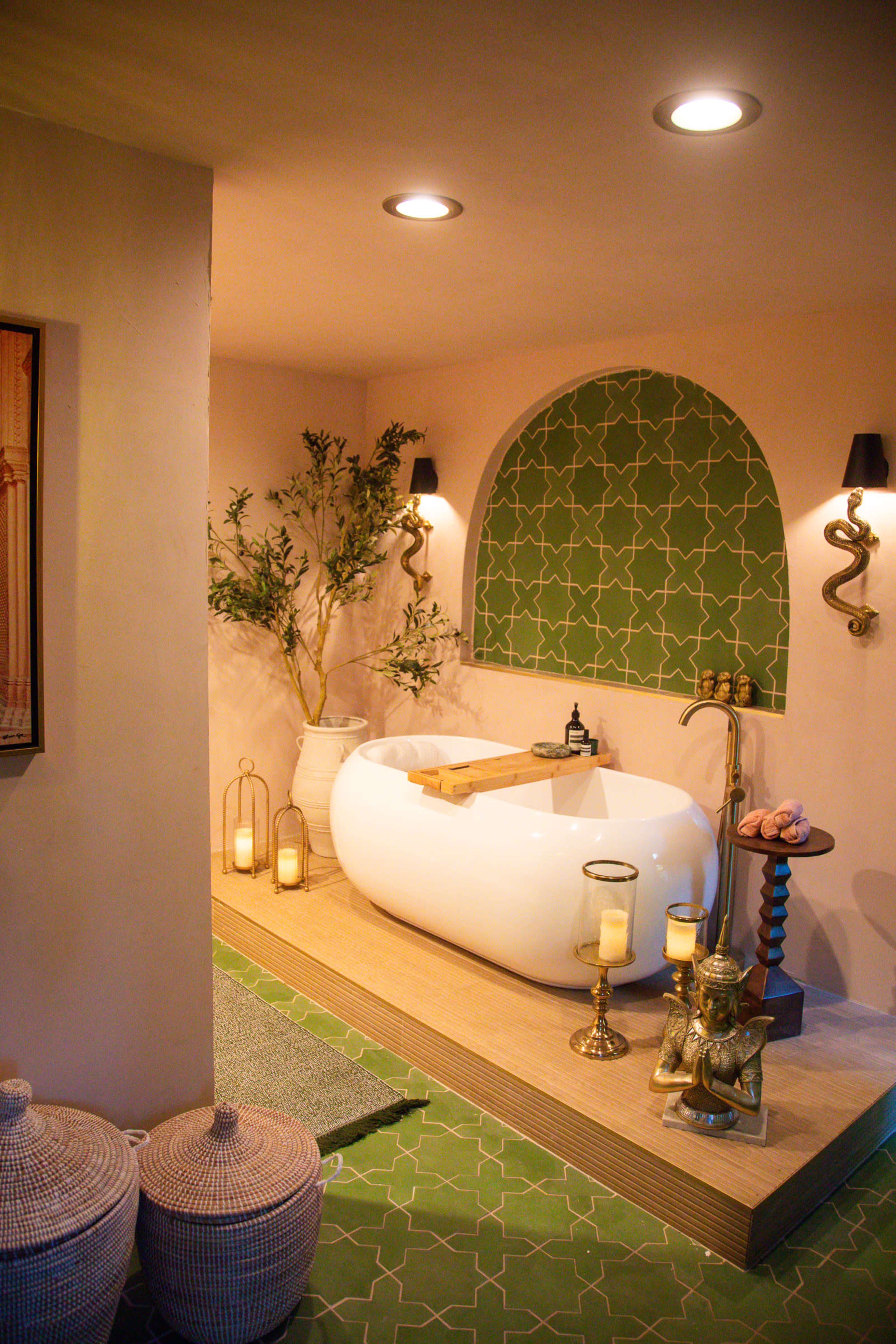The image features a modern bathroom with a freestanding white bathtub, green tiled wall, decorative plants, and various candles arranged around the space.