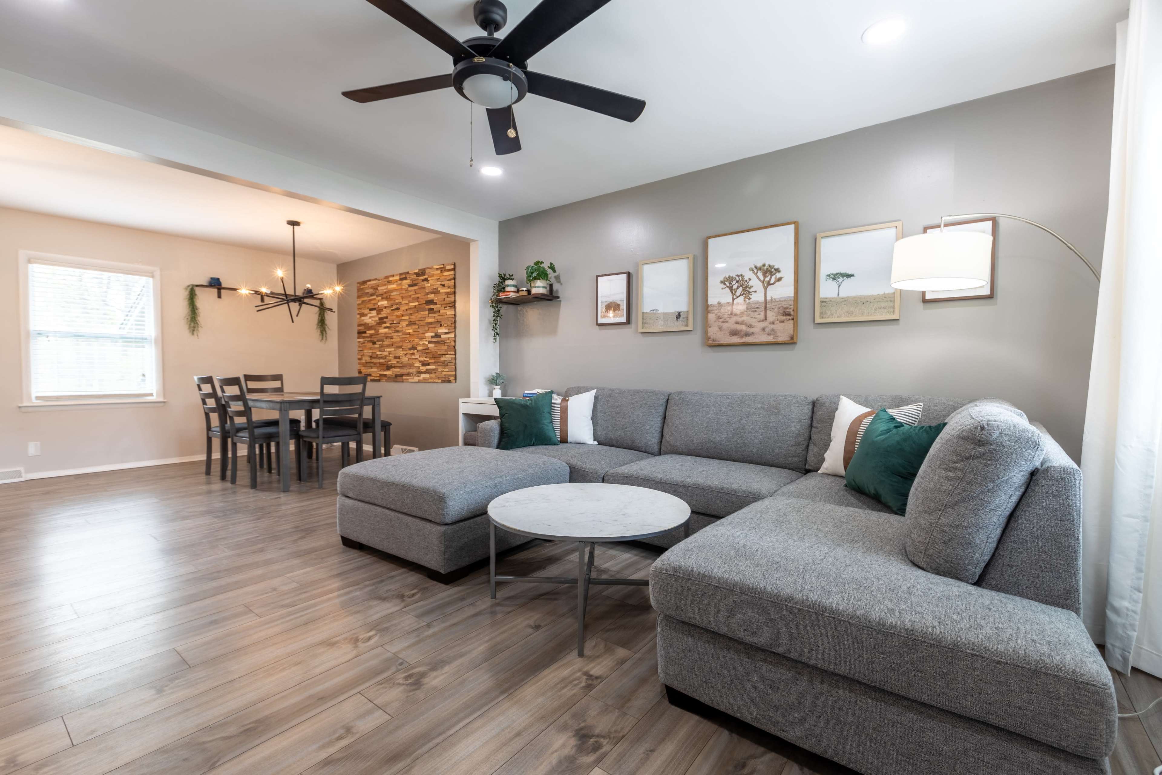 The room features a modern gray sectional sofa, a round coffee table, and a dining area with a wooden table and chairs in an open layout.