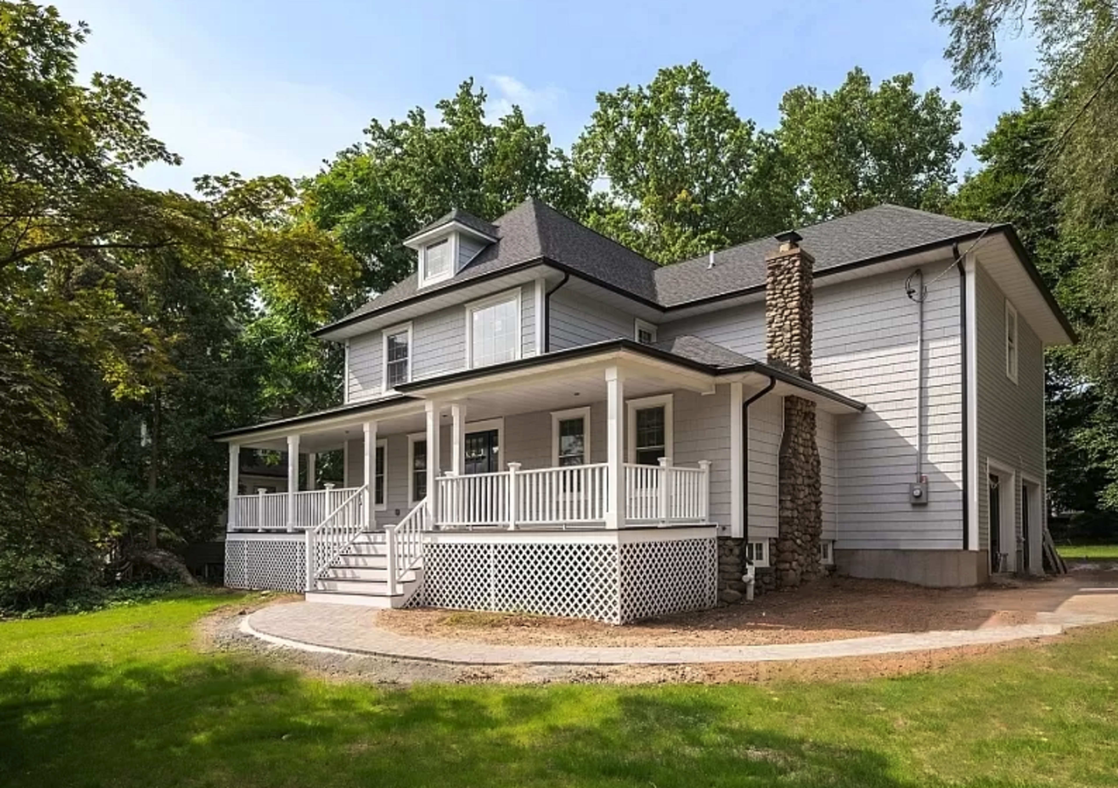 A two-story house with a wraparound porch, surrounded by greenery and a stone pathway.