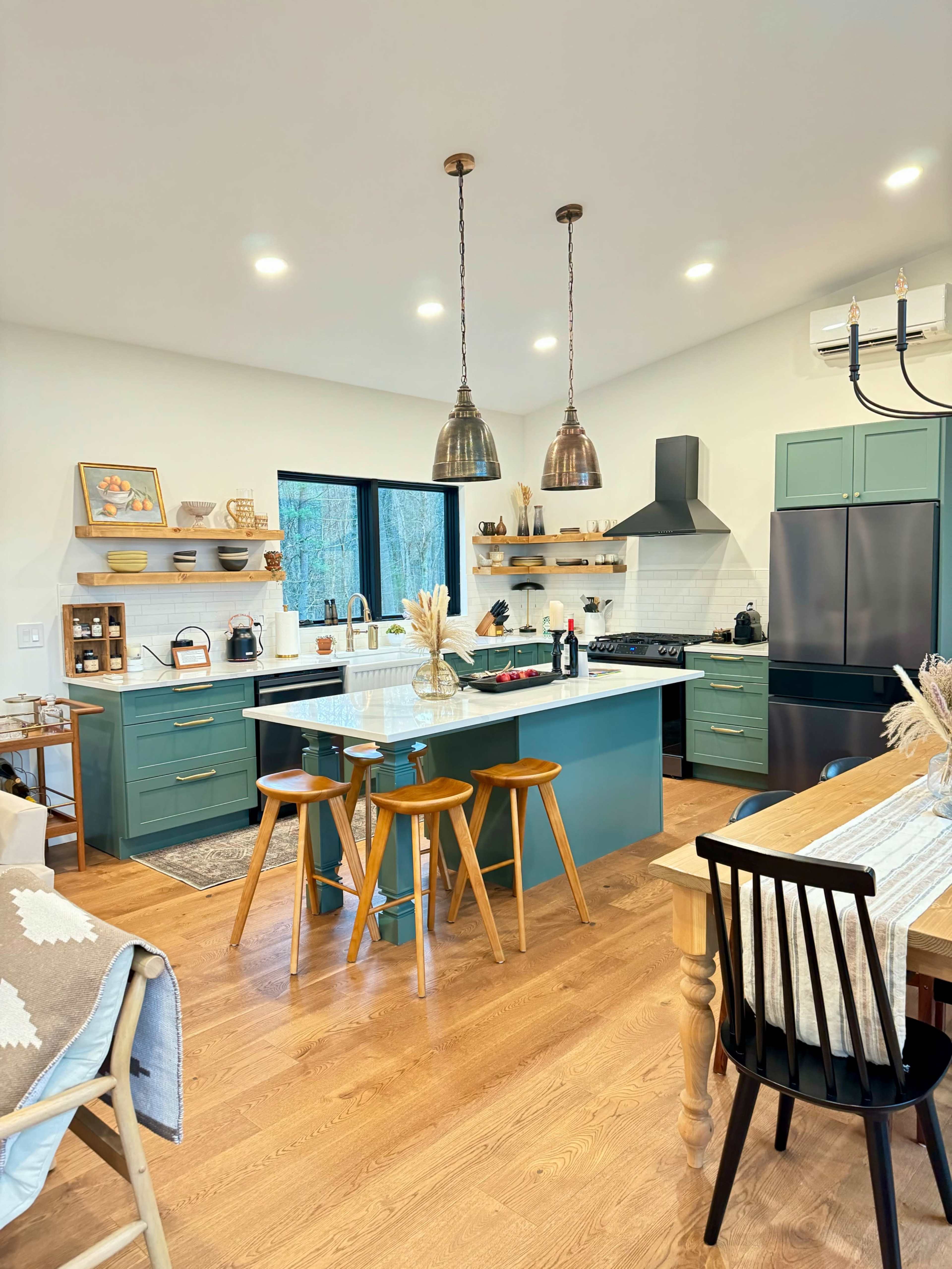 The image shows a modern kitchen featuring teal cabinetry, a central island with bar stools, and hanging pendant lights.