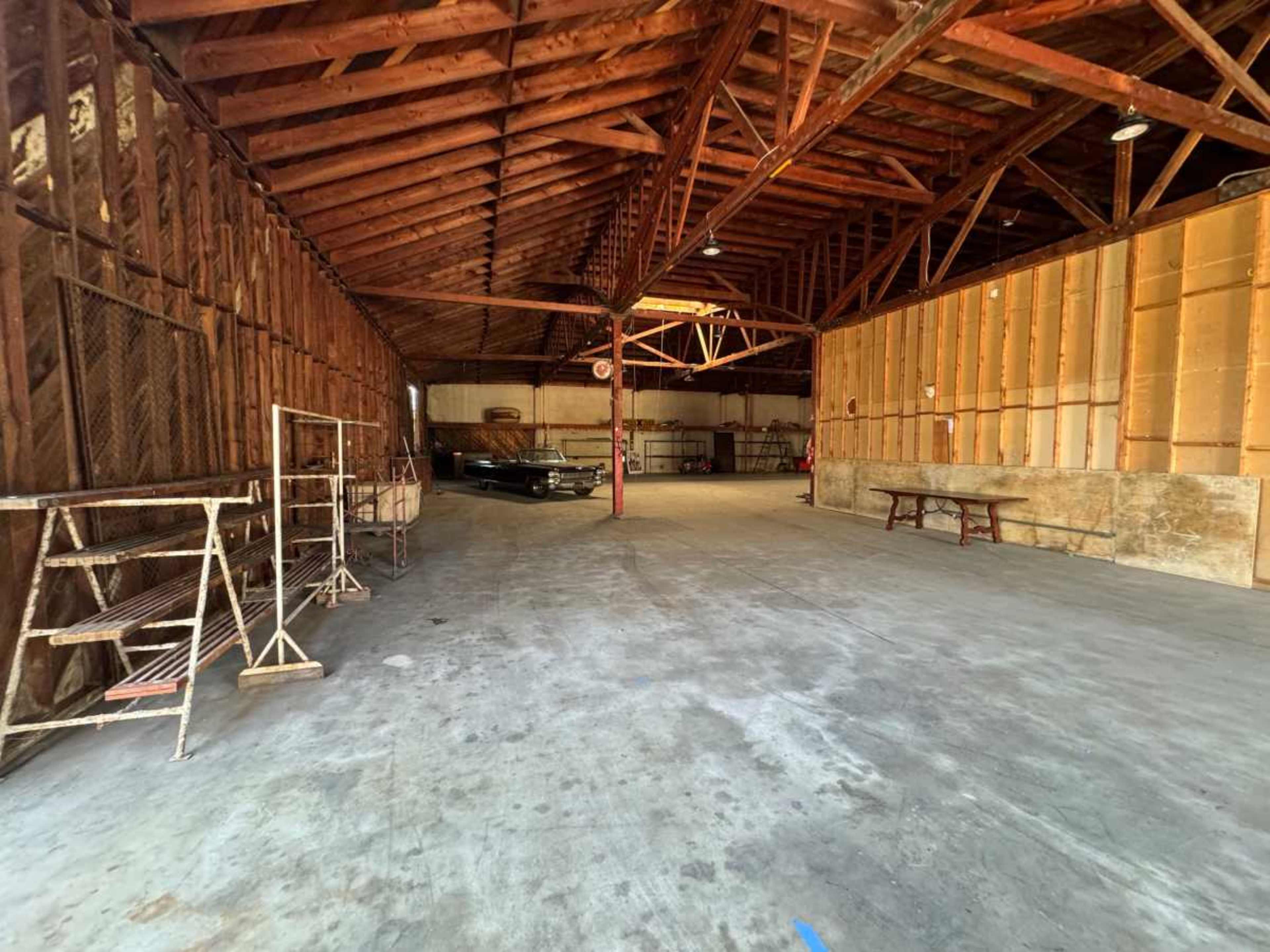 The image shows the interior of a large, empty warehouse with wooden beams and a concrete floor.