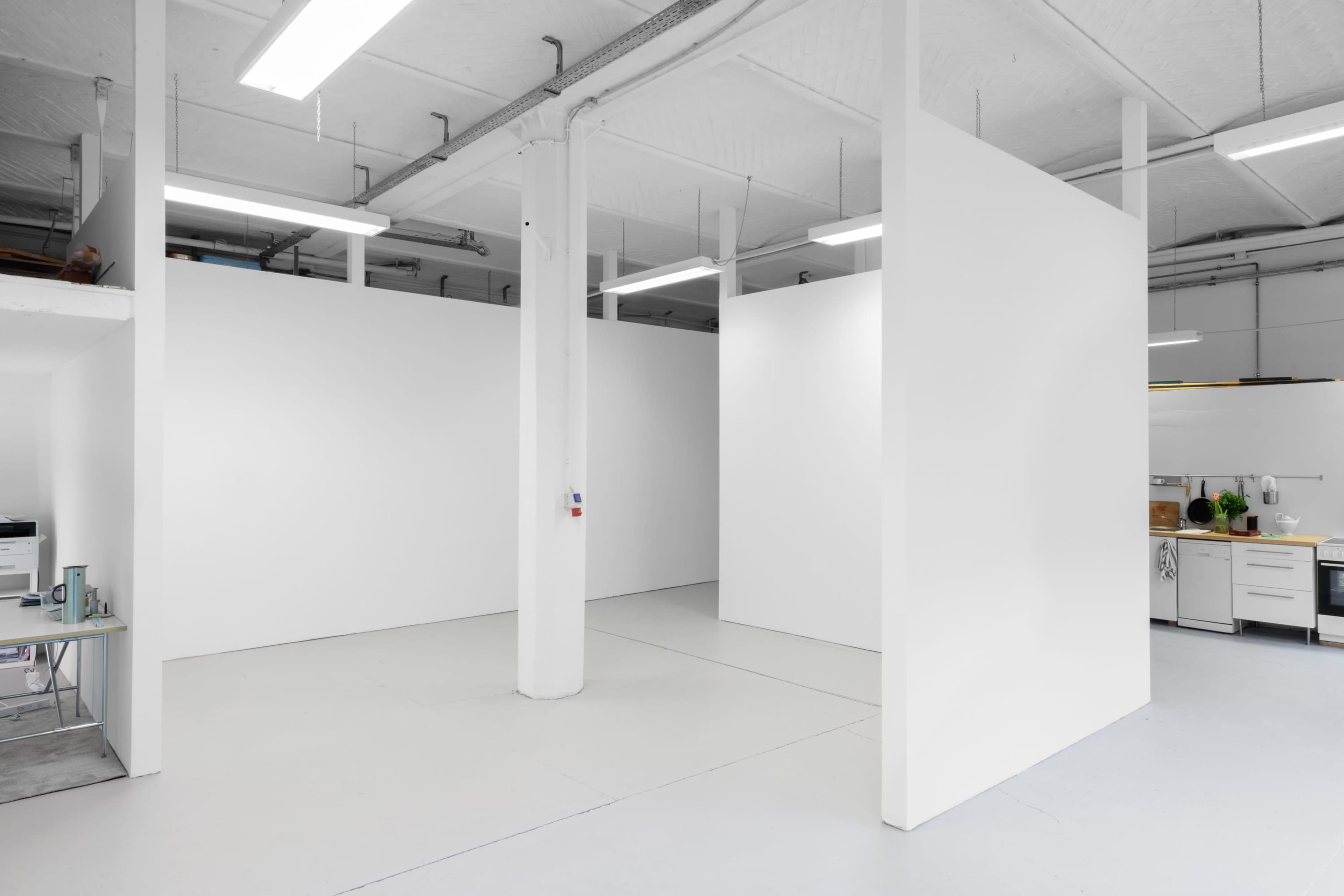 A spacious, empty room with white walls, a polished floor, and multiple vertical partitions creating distinct areas.