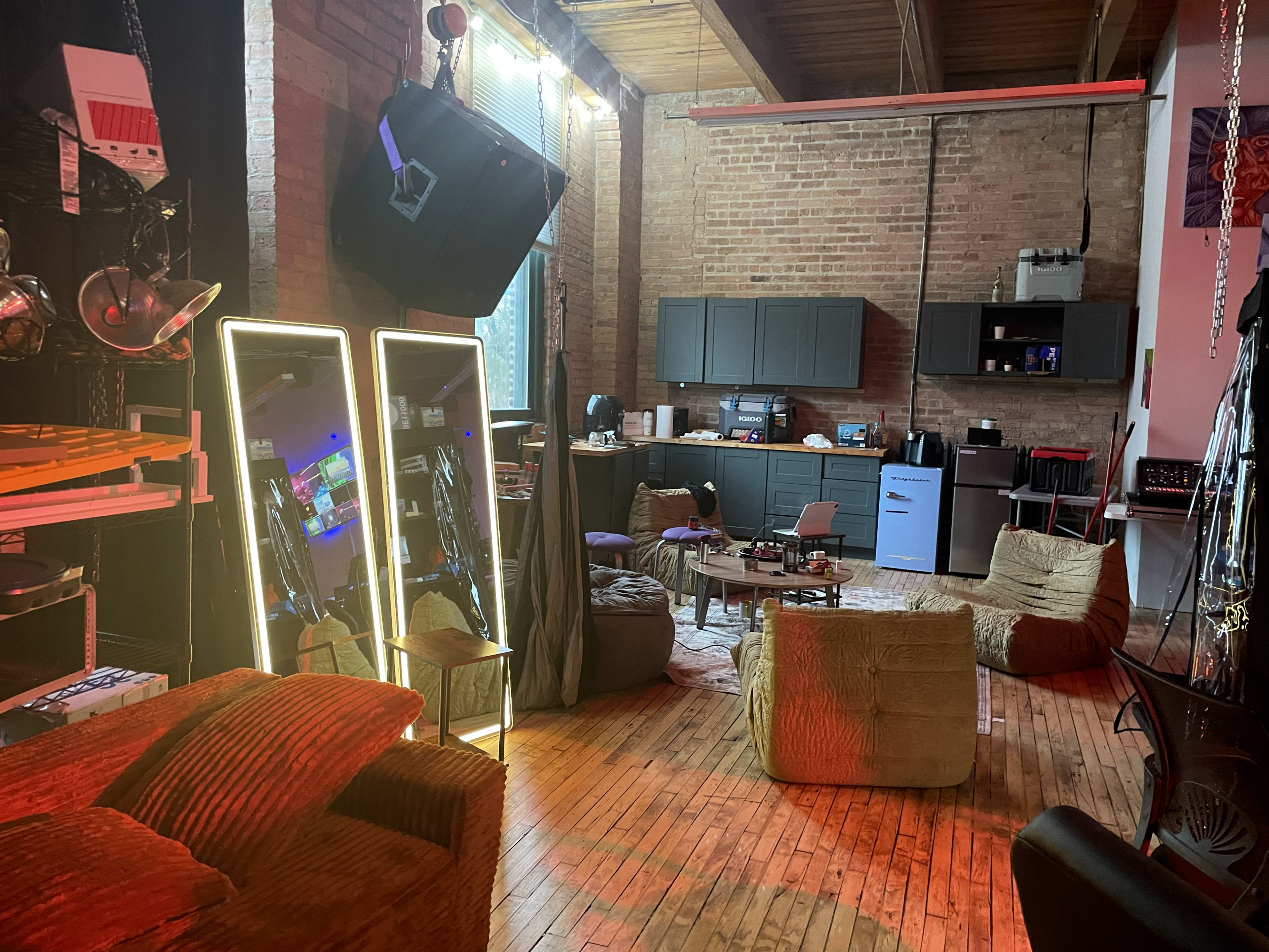 The image shows an industrial-style lounge area featuring two large mirrors, a kitchenette, several bean bag chairs, and a mix of modern and vintage decor.