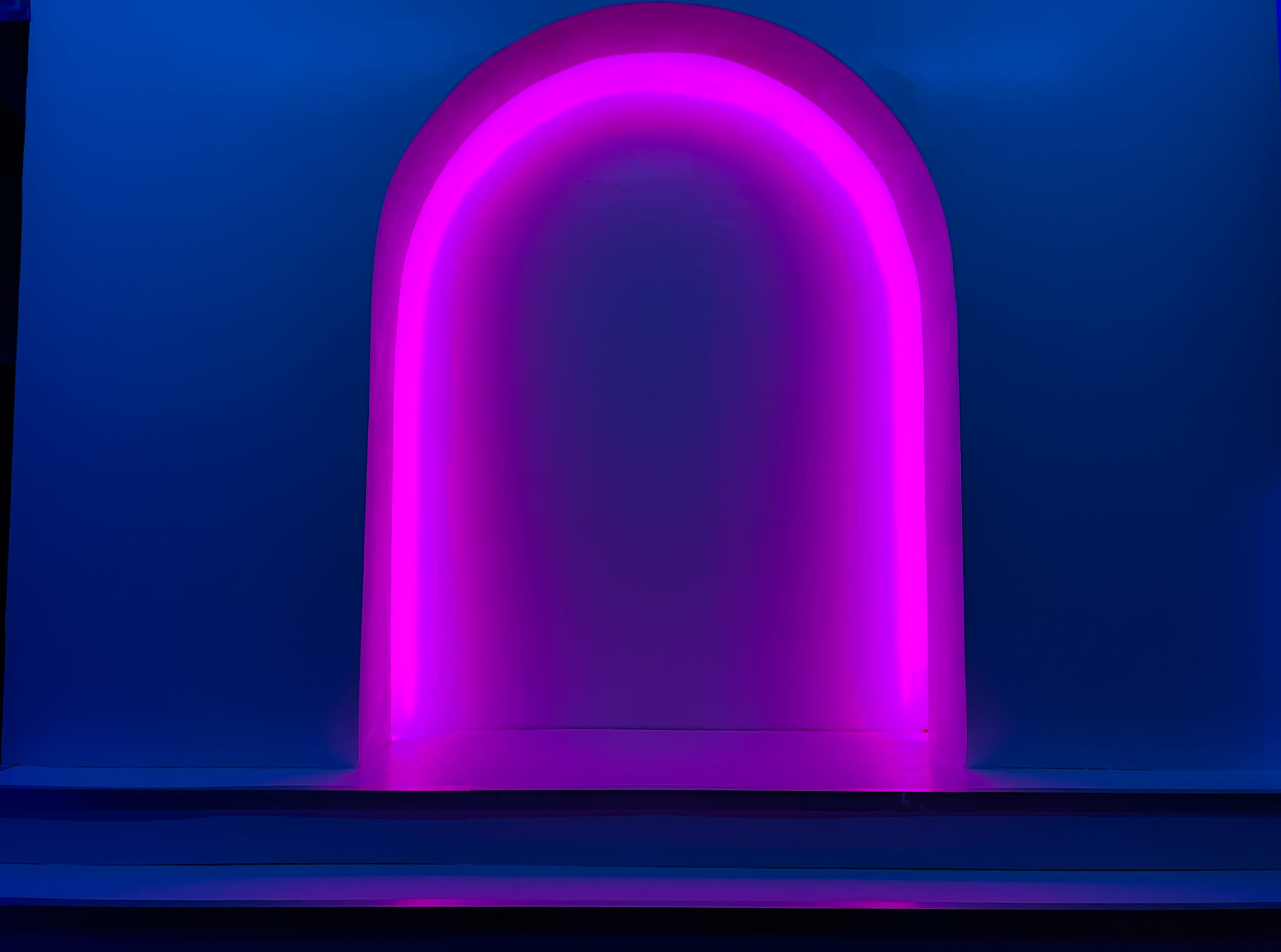 A curved neon light in pink illuminates an archway against a blue background.