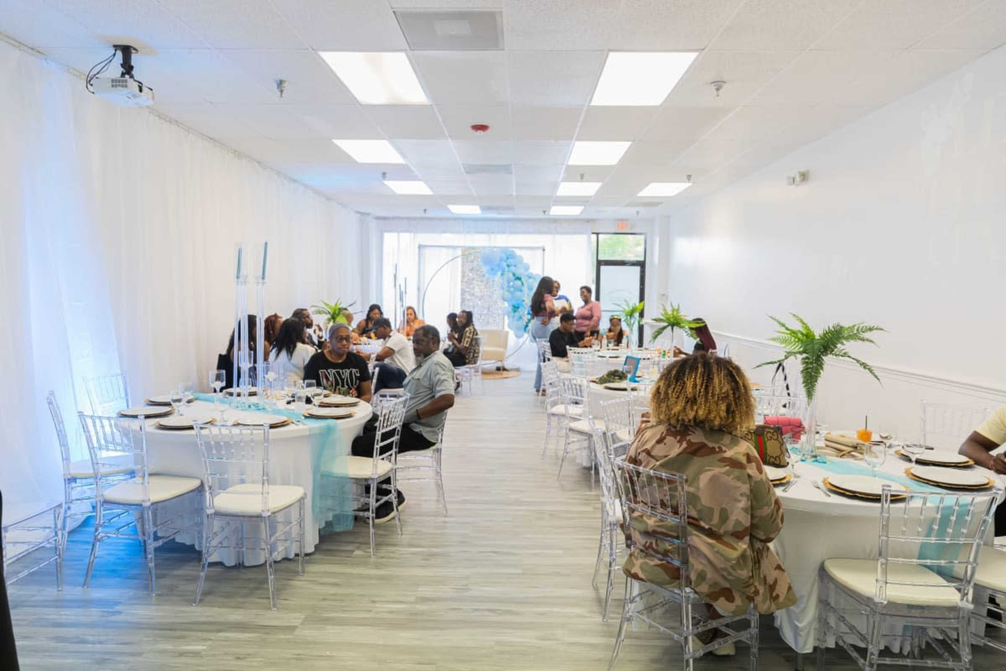 The image shows a bright, modern event space with tables set for dining and guests socializing.