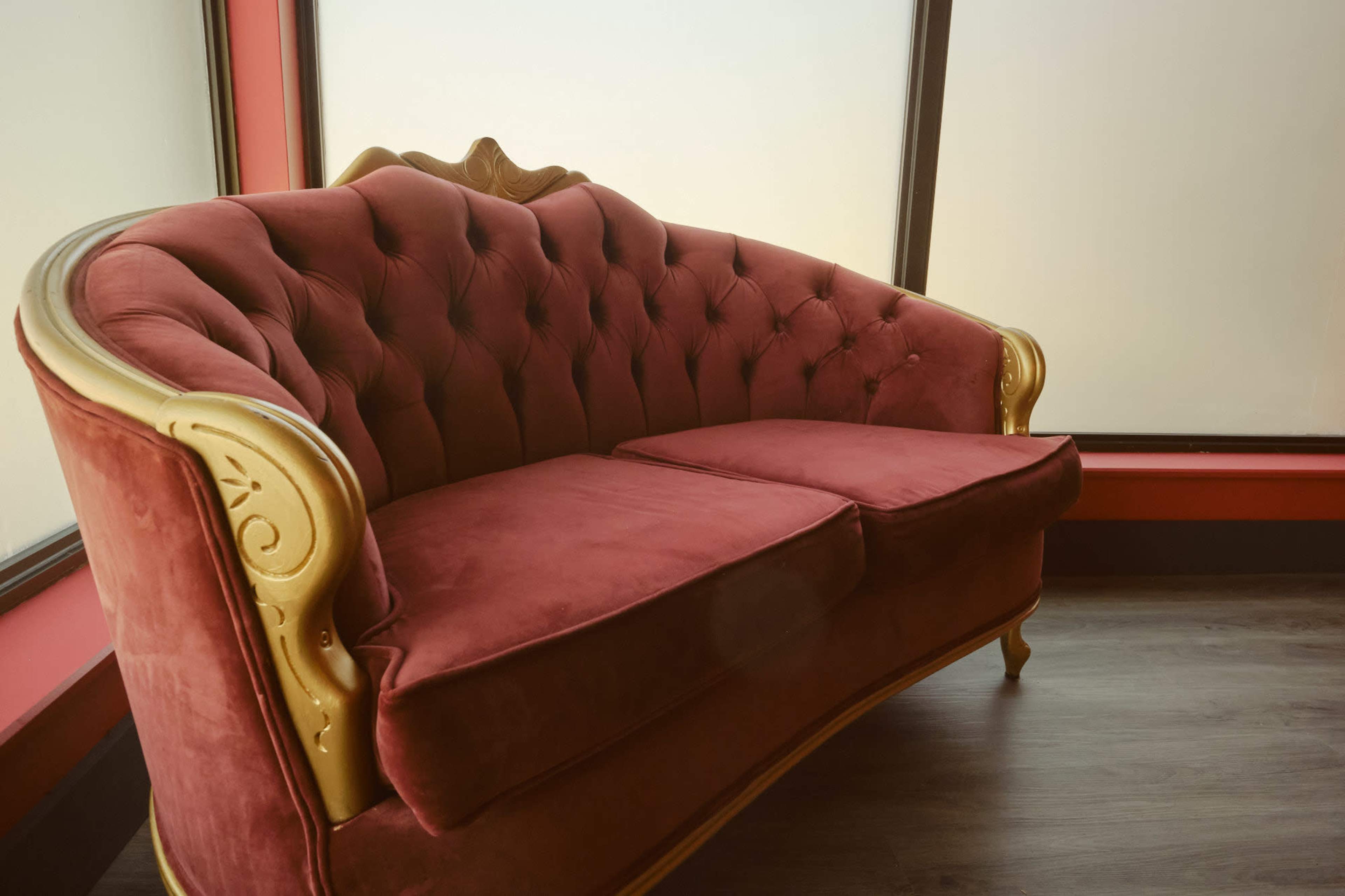 A vintage-style red velvet sofa with gold accents is positioned beside a large frosted window.