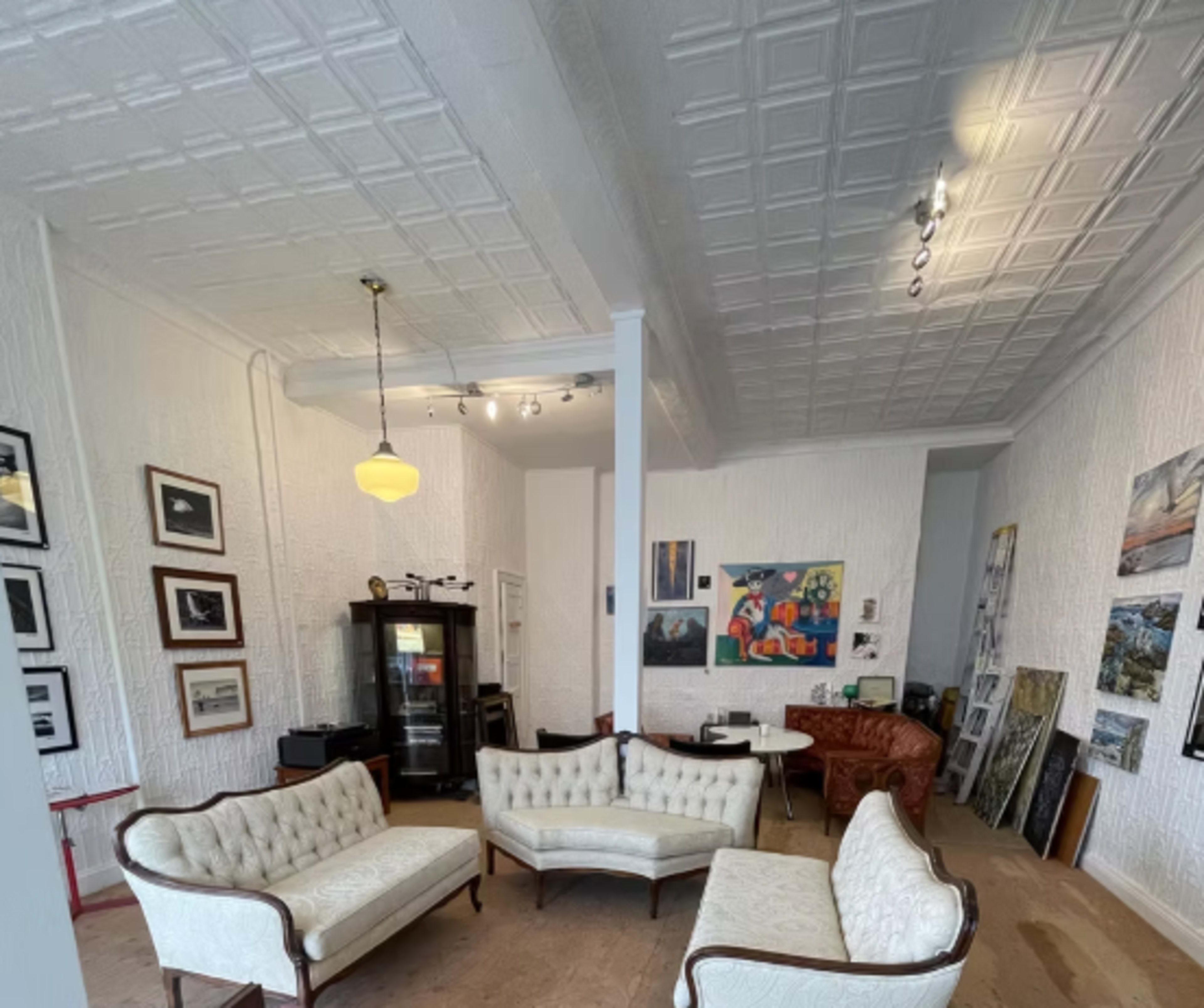 The image shows a gallery-like interior with vintage furniture, framed artworks on the walls, and a mix of seating arrangements.