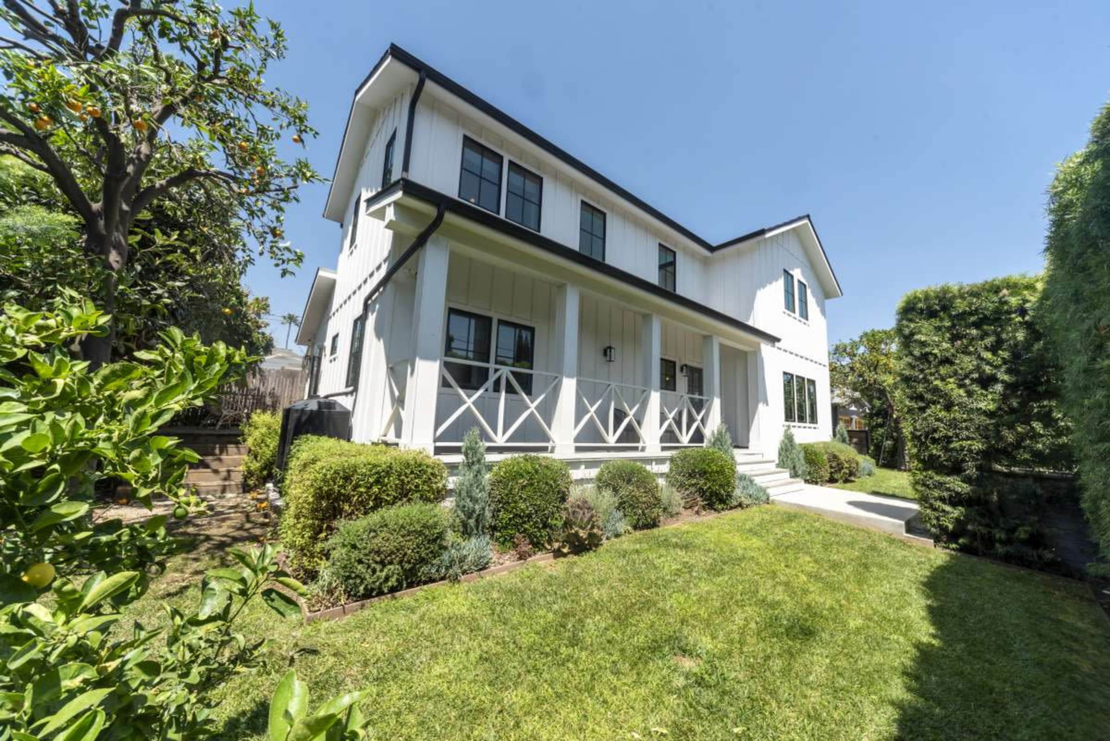 A two-story white house with black trim stands in a well-maintained yard surrounded by trimmed hedges and a pathway leading to the front door.