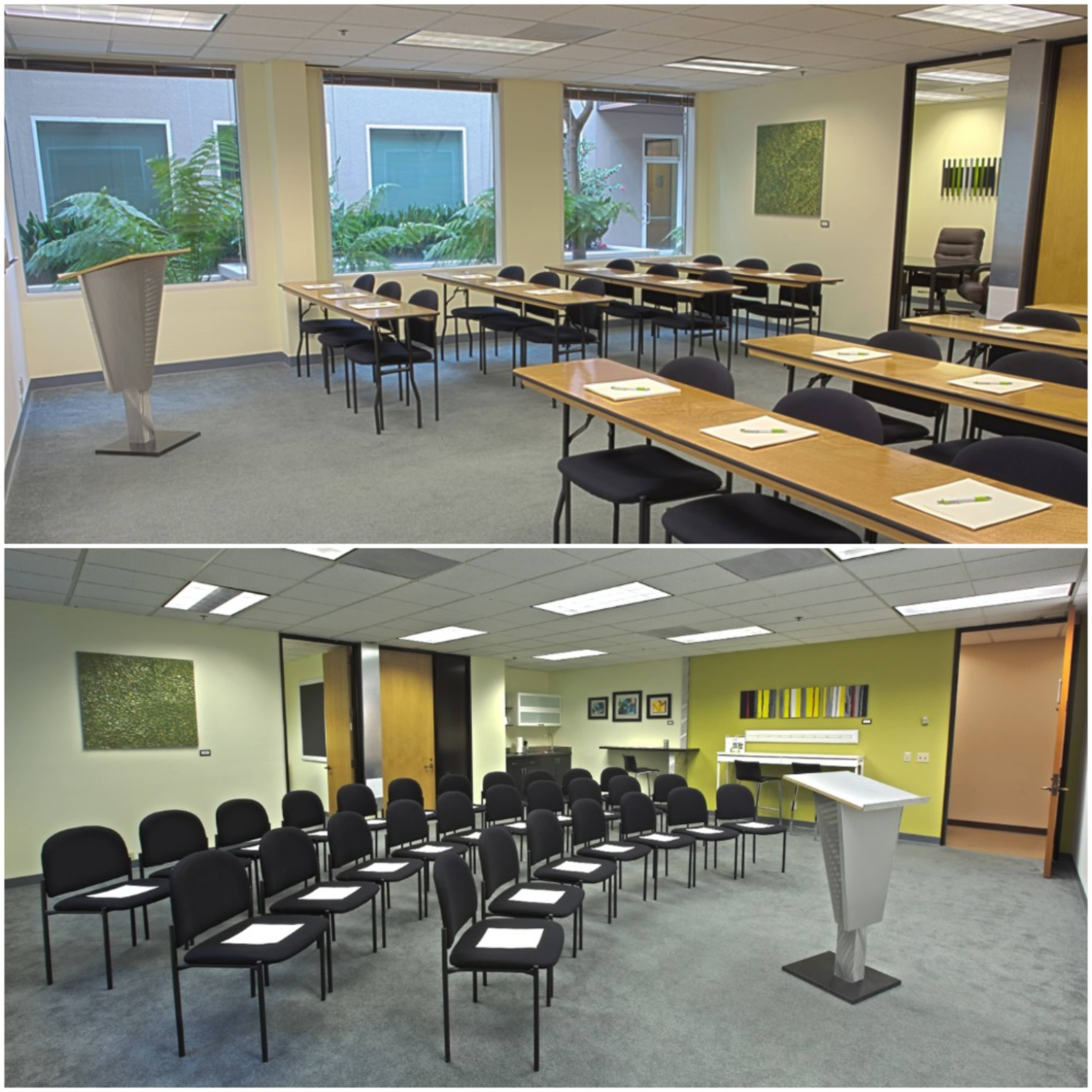 A conference room set up with tables arranged in a U-shape and chairs facing a podium, featuring large windows and green artwork on the walls.