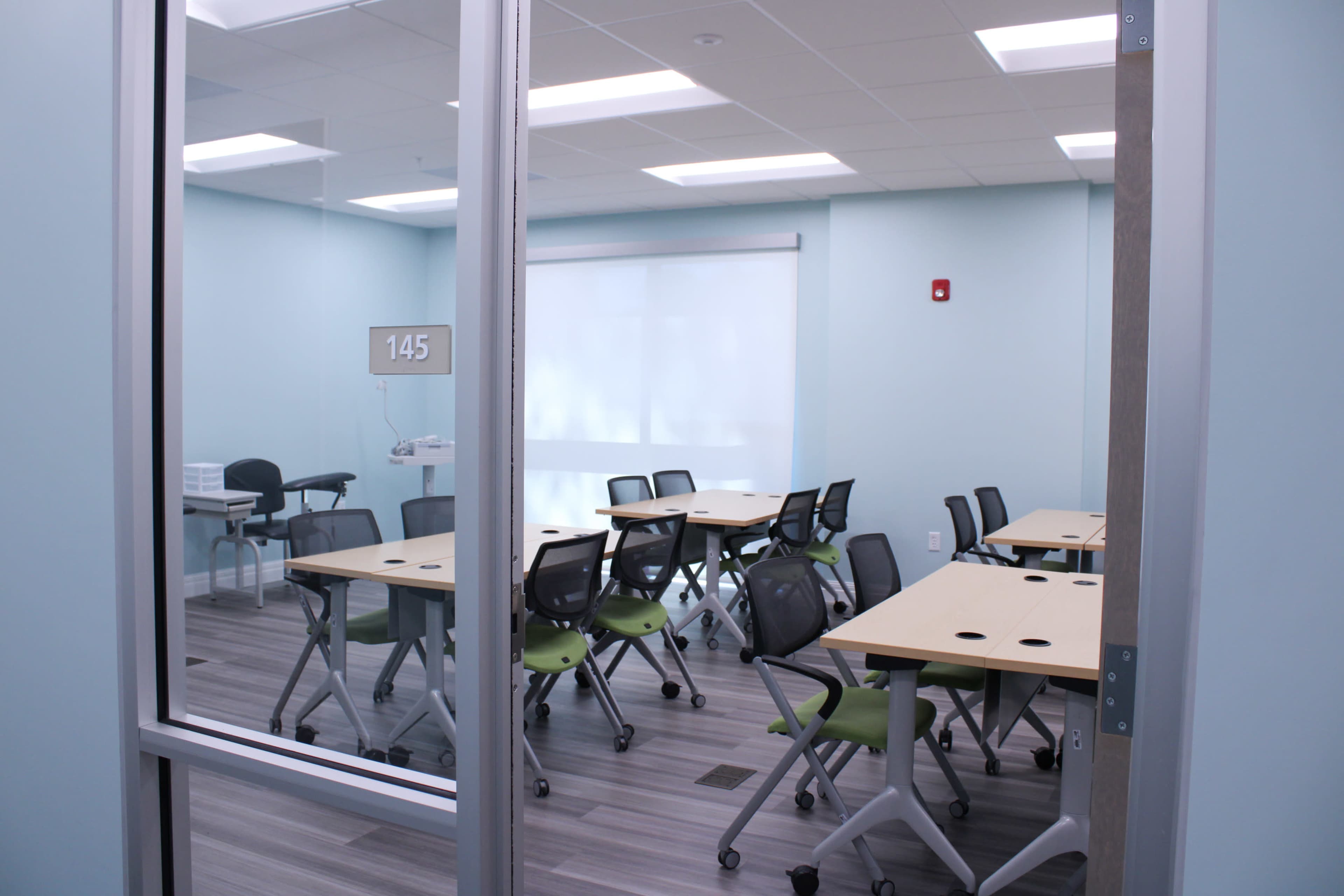 A classroom with several movable tables and chairs arranged in a tidy manner, illuminated by overhead lights.