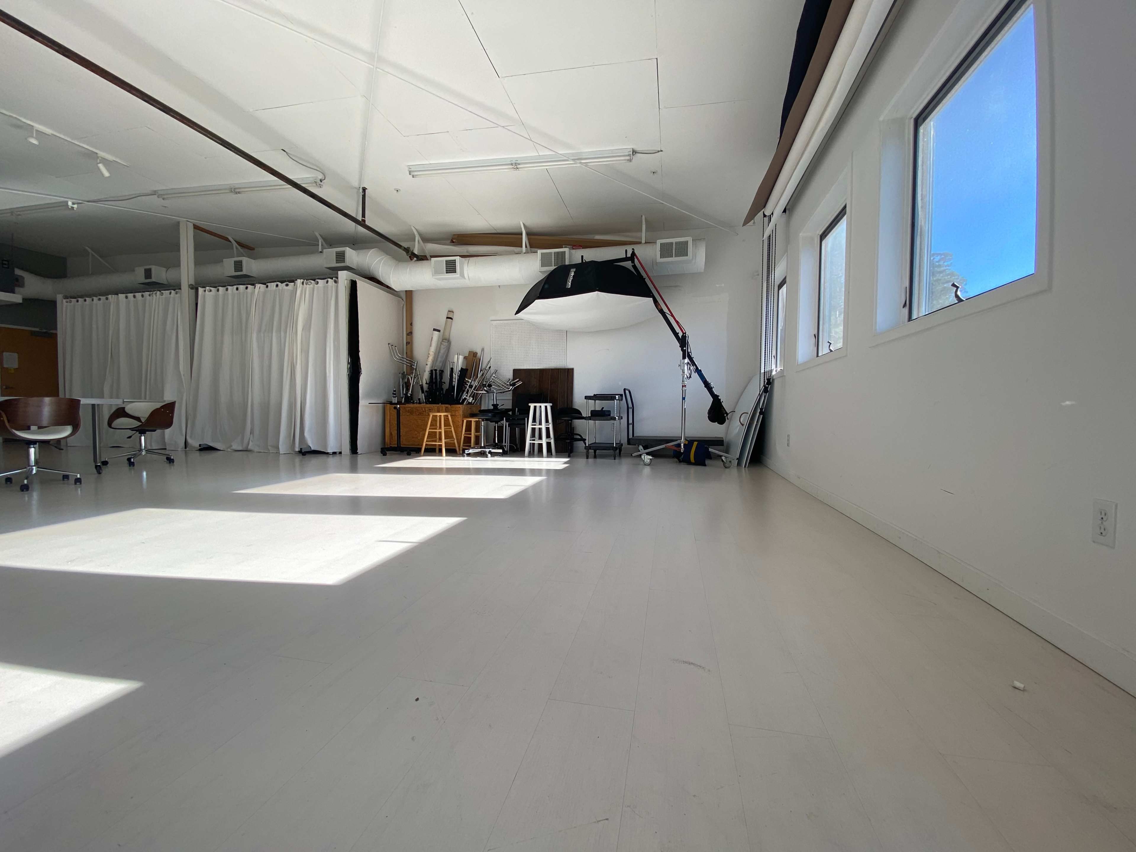 A bright, spacious studio with white walls, wooden furniture, and a large softbox light on a stand.
