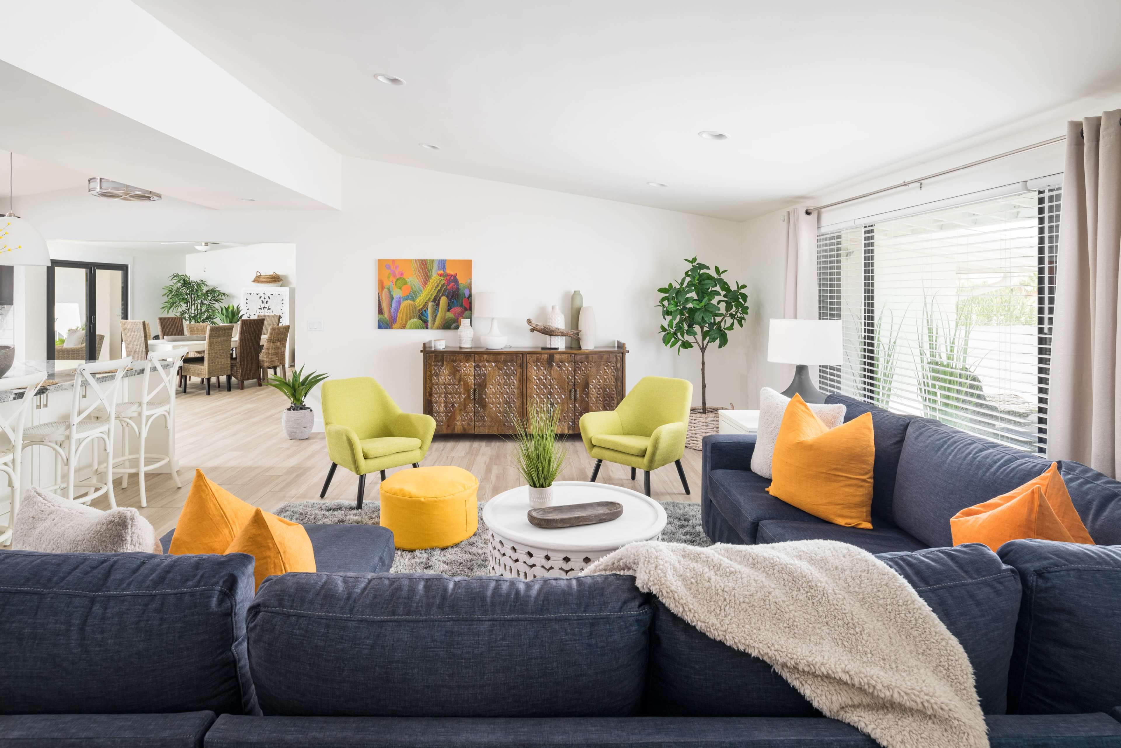 The image shows a contemporary living room with a dark blue sectional sofa, bright green chairs, orange accent pillows, and a round coffee table, all arranged around a textured area rug.