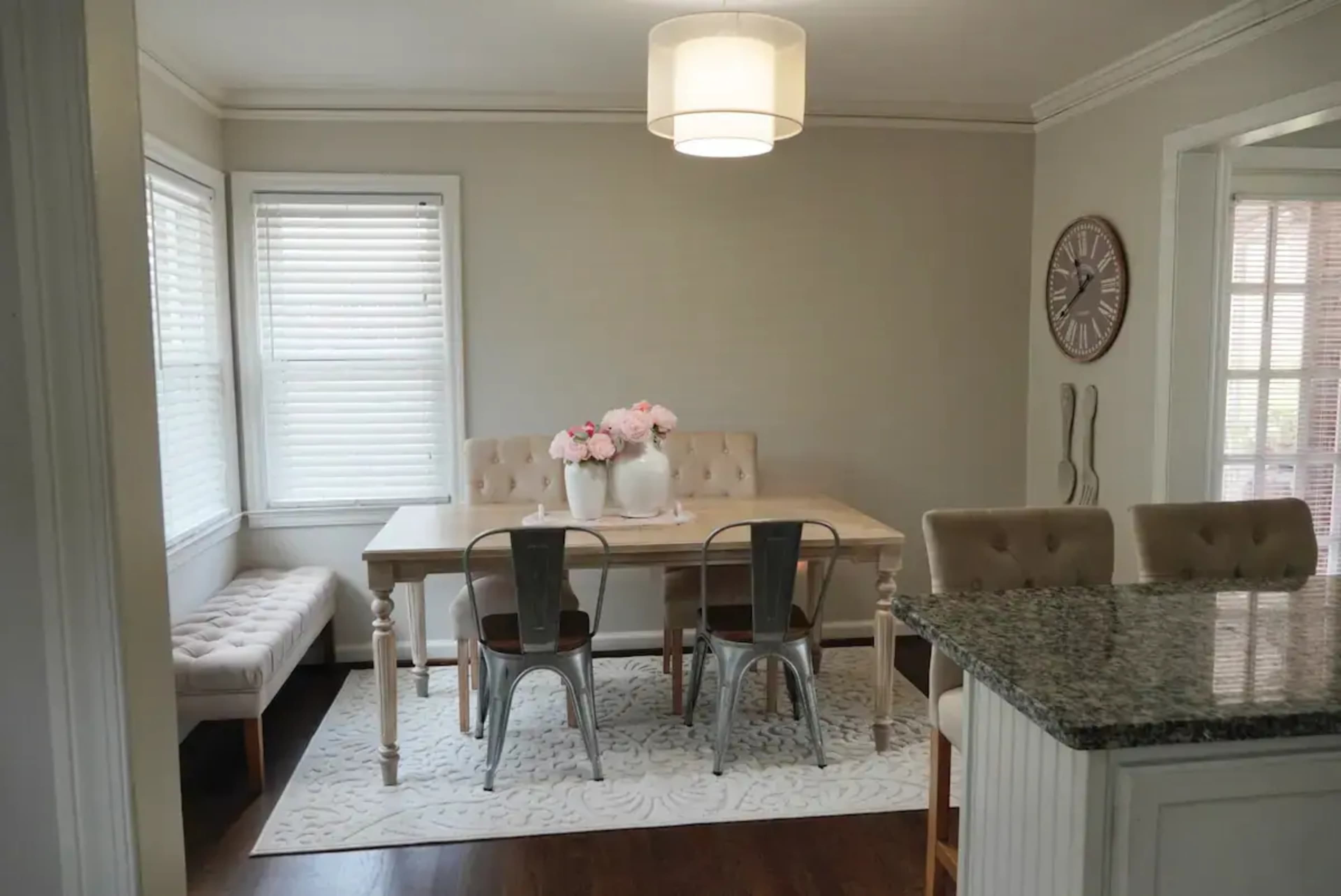 A dining area features a light-colored table surrounded by chairs, with a cozy bench along one wall and a light fixture above.