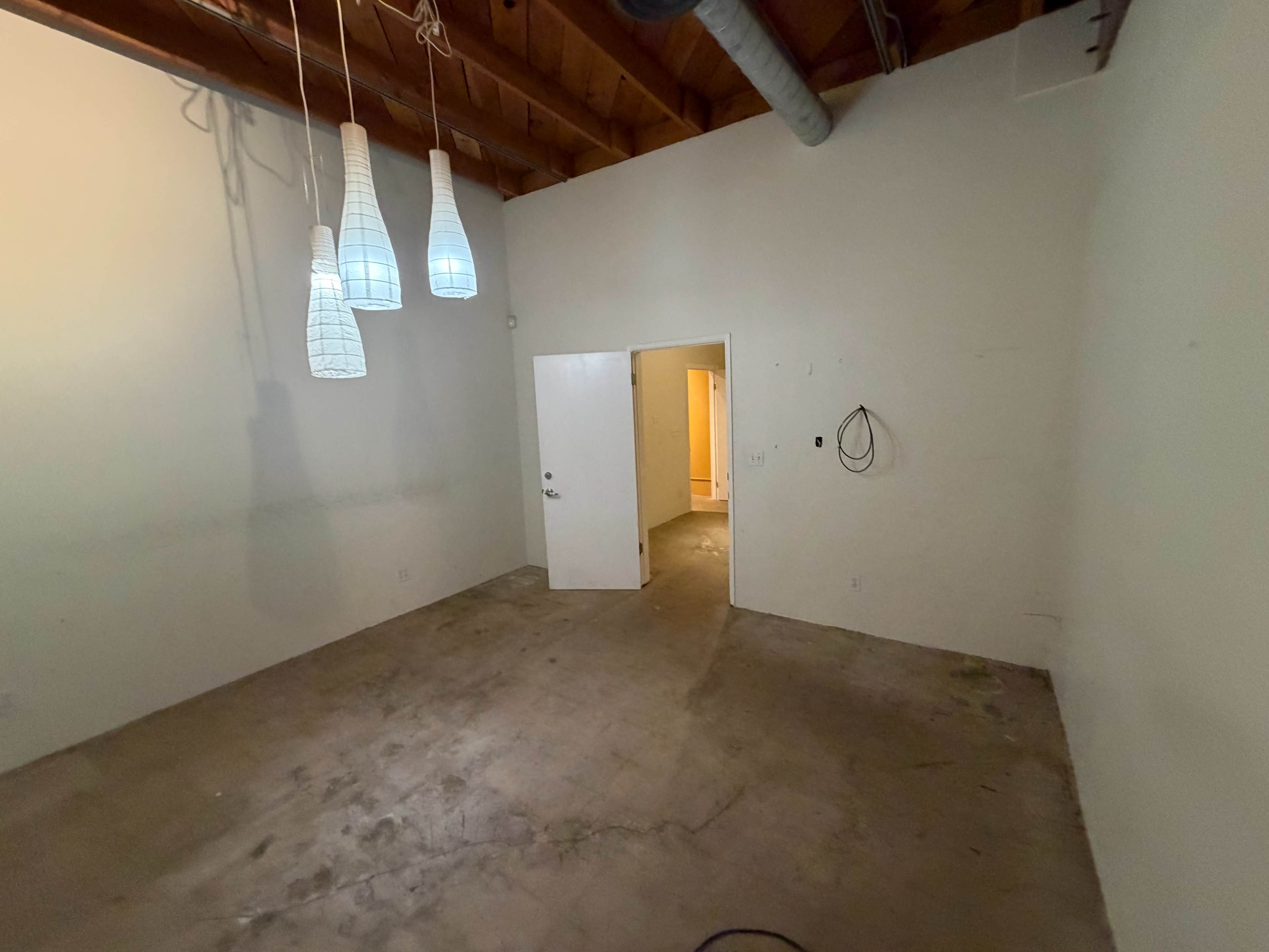 The image shows an empty room with beige walls, a concrete floor, and three pendant lights hanging from the ceiling.