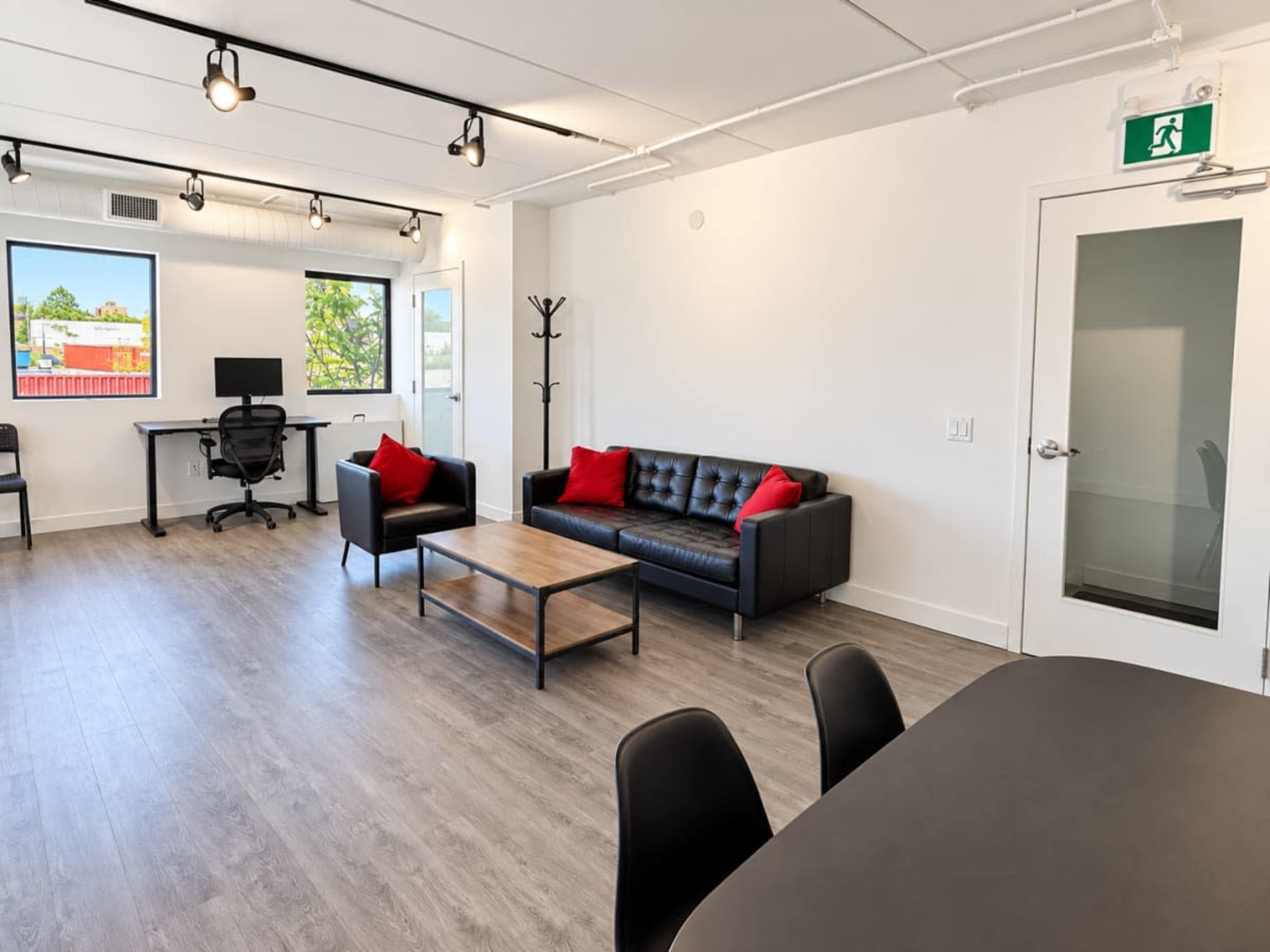 The image shows a modern office space with a black leather sofa, a coffee table, and a desk in a well-lit setting.