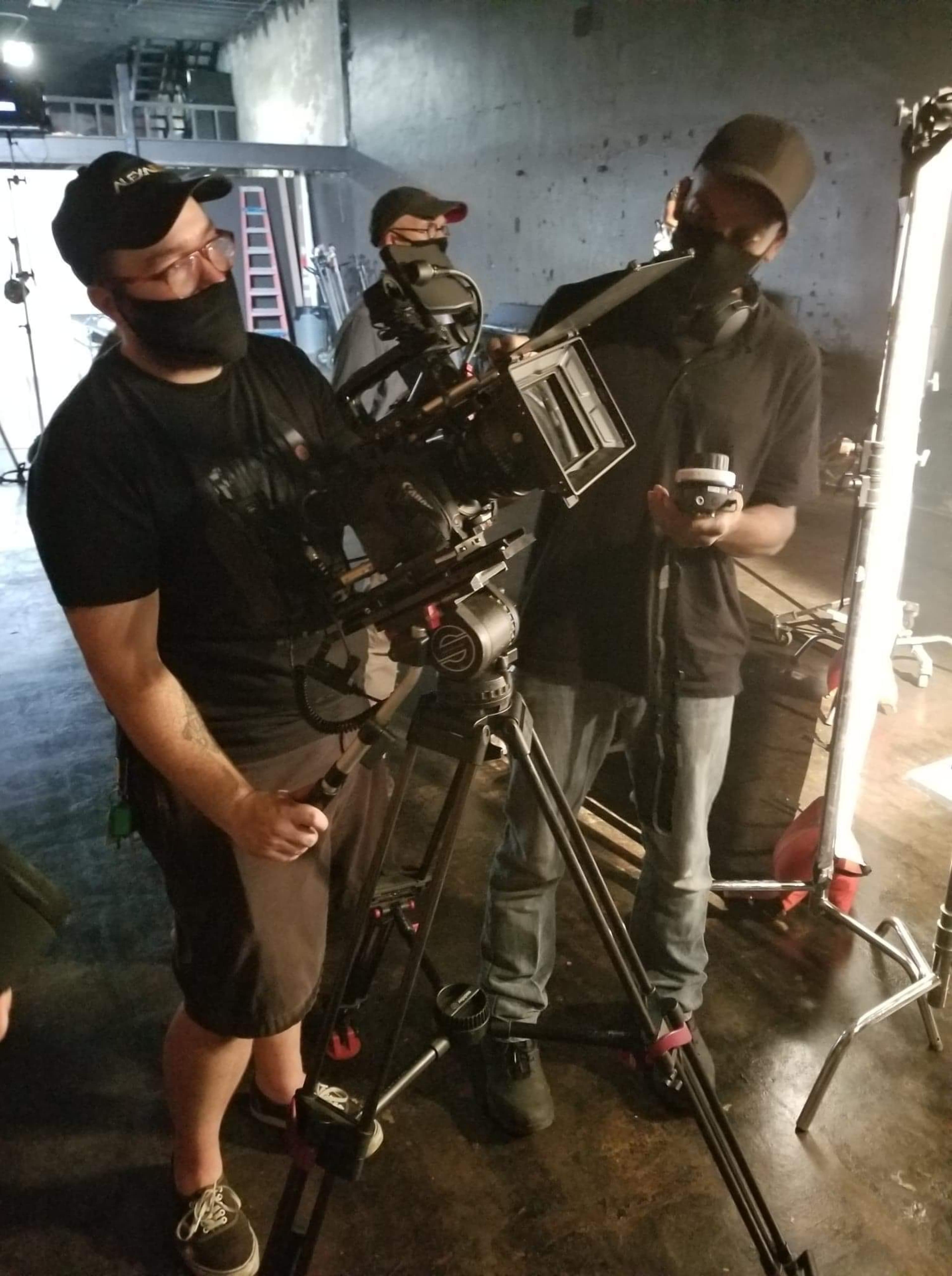 Two filmmakers are setting up a camera on a tripod in a dimly lit studio.