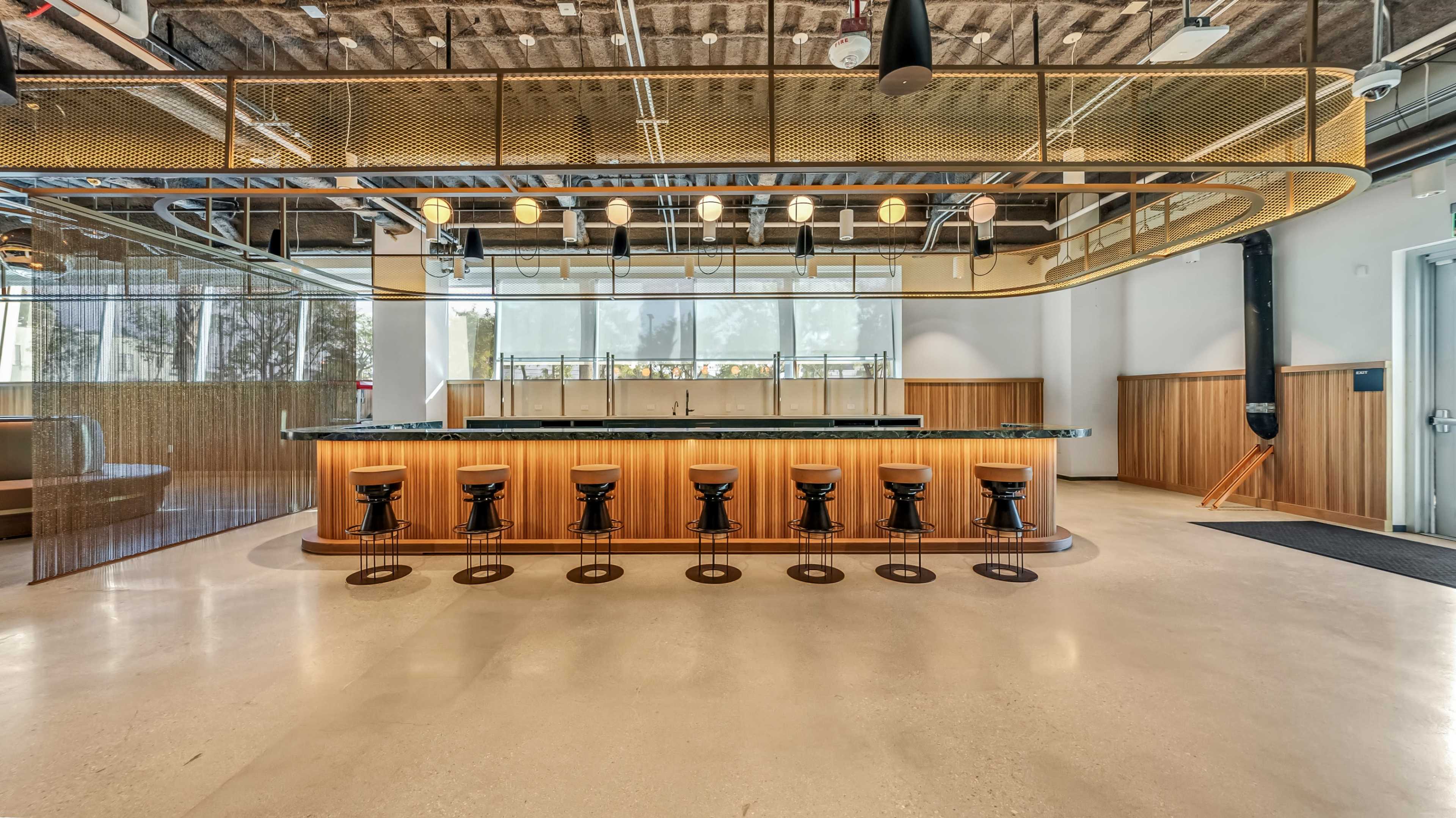 A modern bar area with a curved wooden counter and several black stools arranged in front of it.