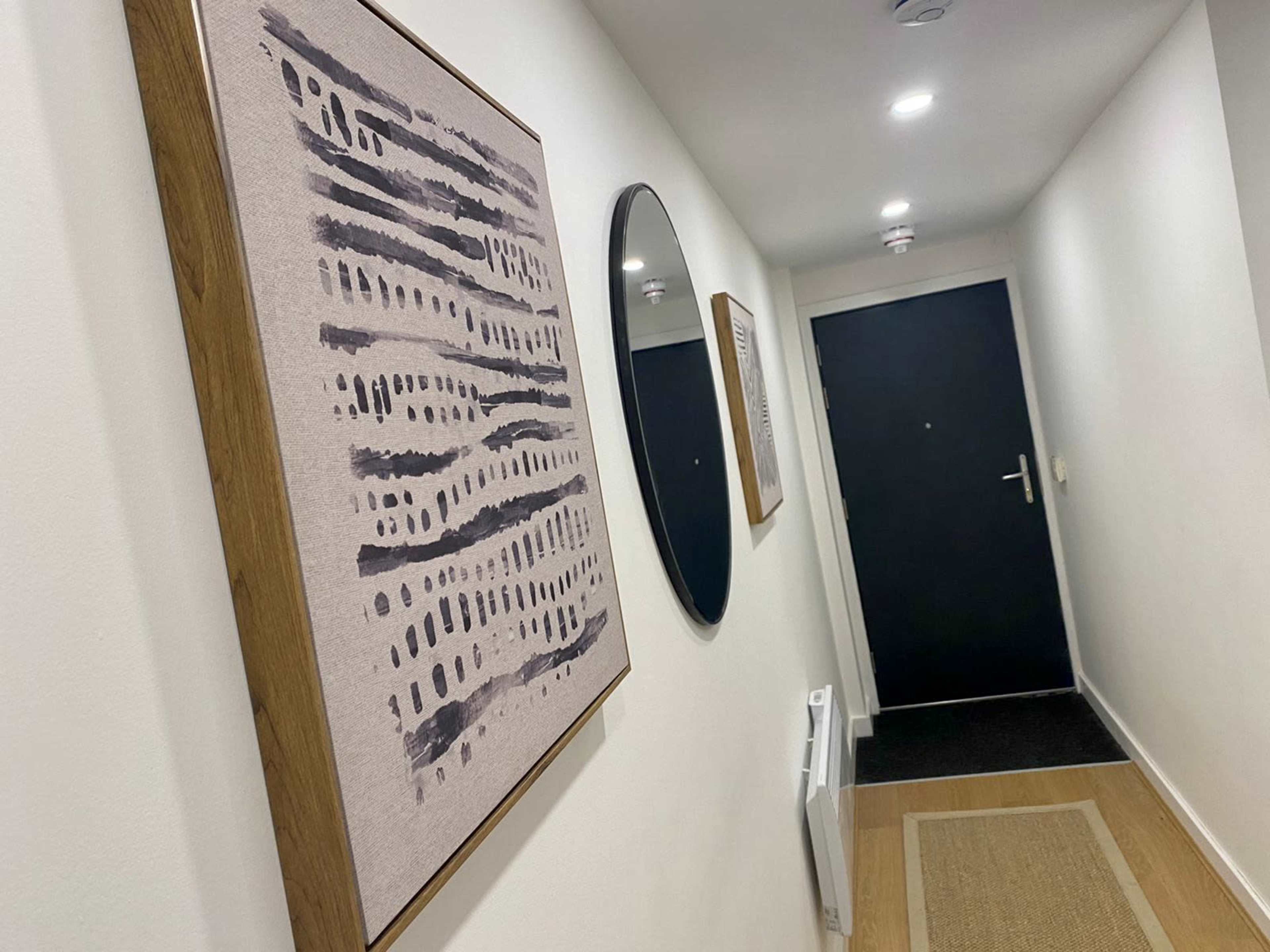 A narrow hallway with framed artwork and a round mirror on the walls, leading to a black door at the end.