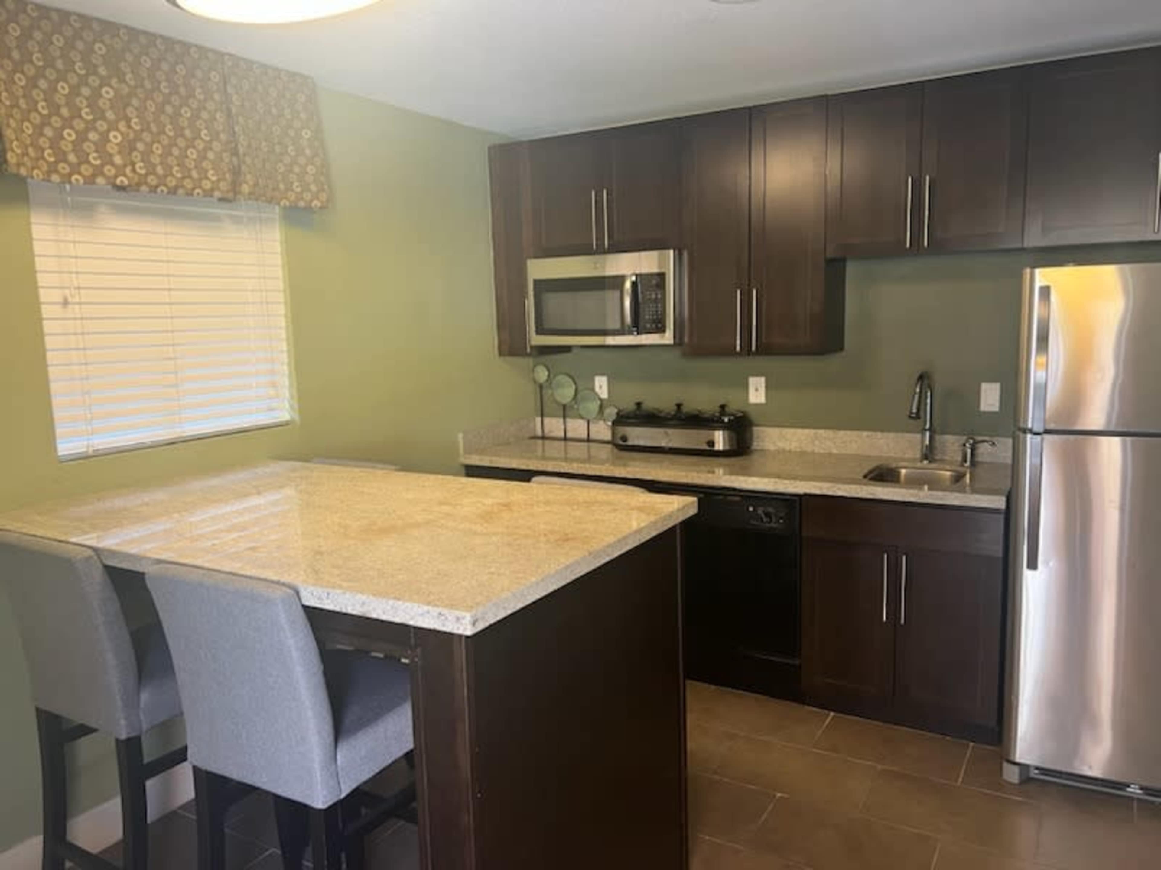 A modern kitchen featuring dark cabinetry, stainless steel appliances, and a granite countertop with bar seating.