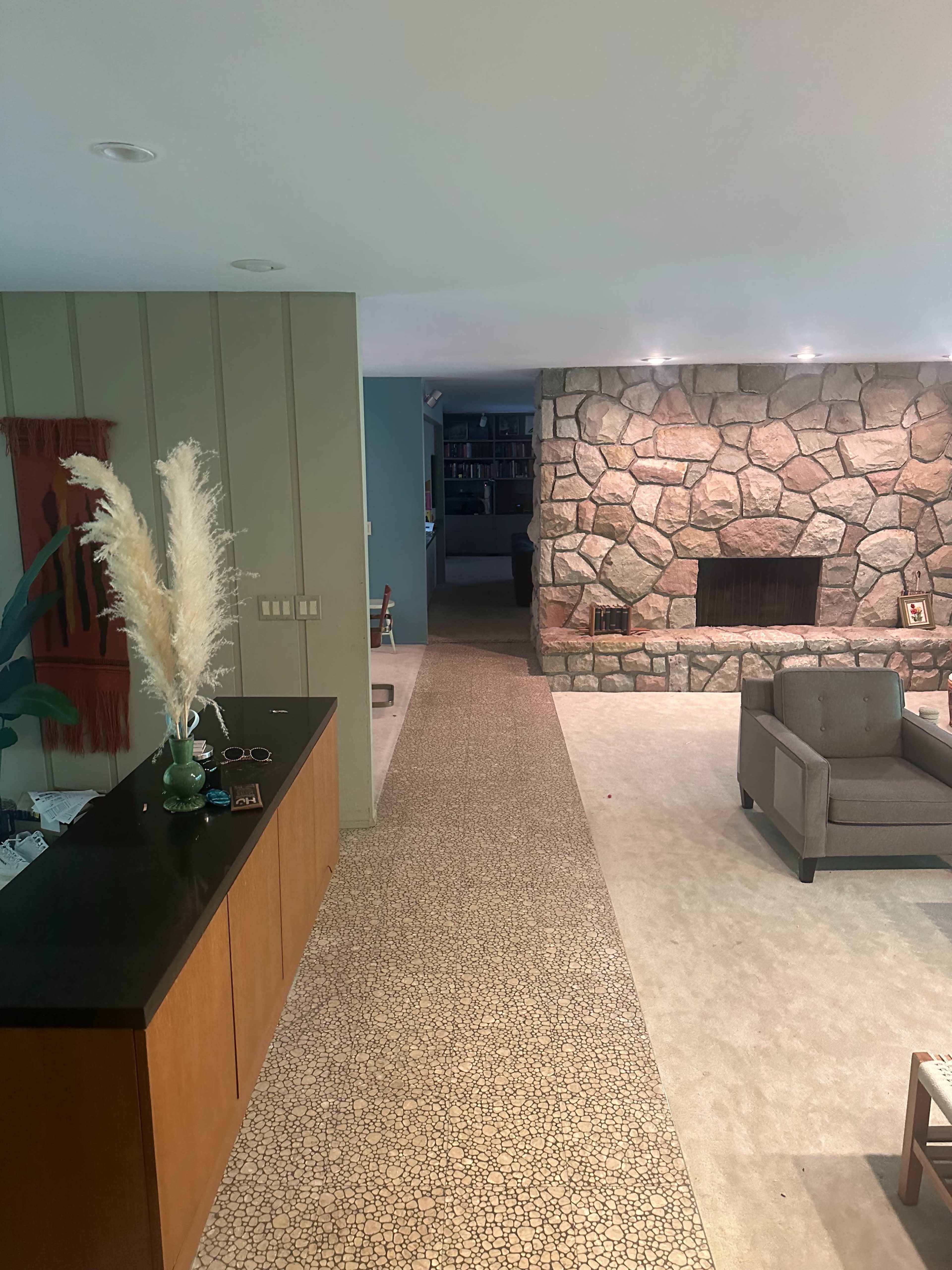The image shows a spacious living area with a stone fireplace, a seating arrangement, and a decorative entryway featuring a console table and a plant.