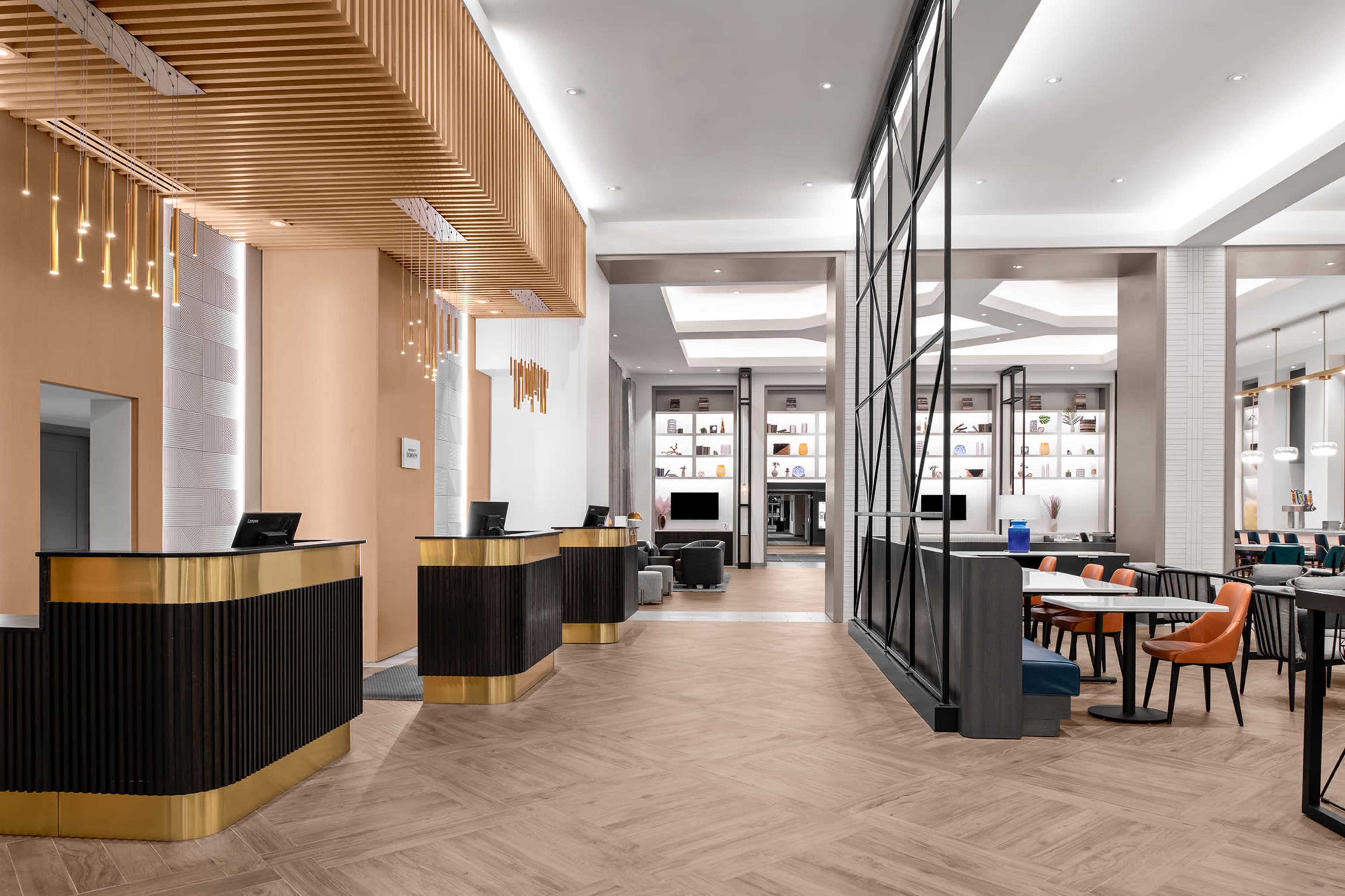 A modern hotel lobby with two reception desks, a dining area featuring tables and chairs, and shelves displaying decorative items.