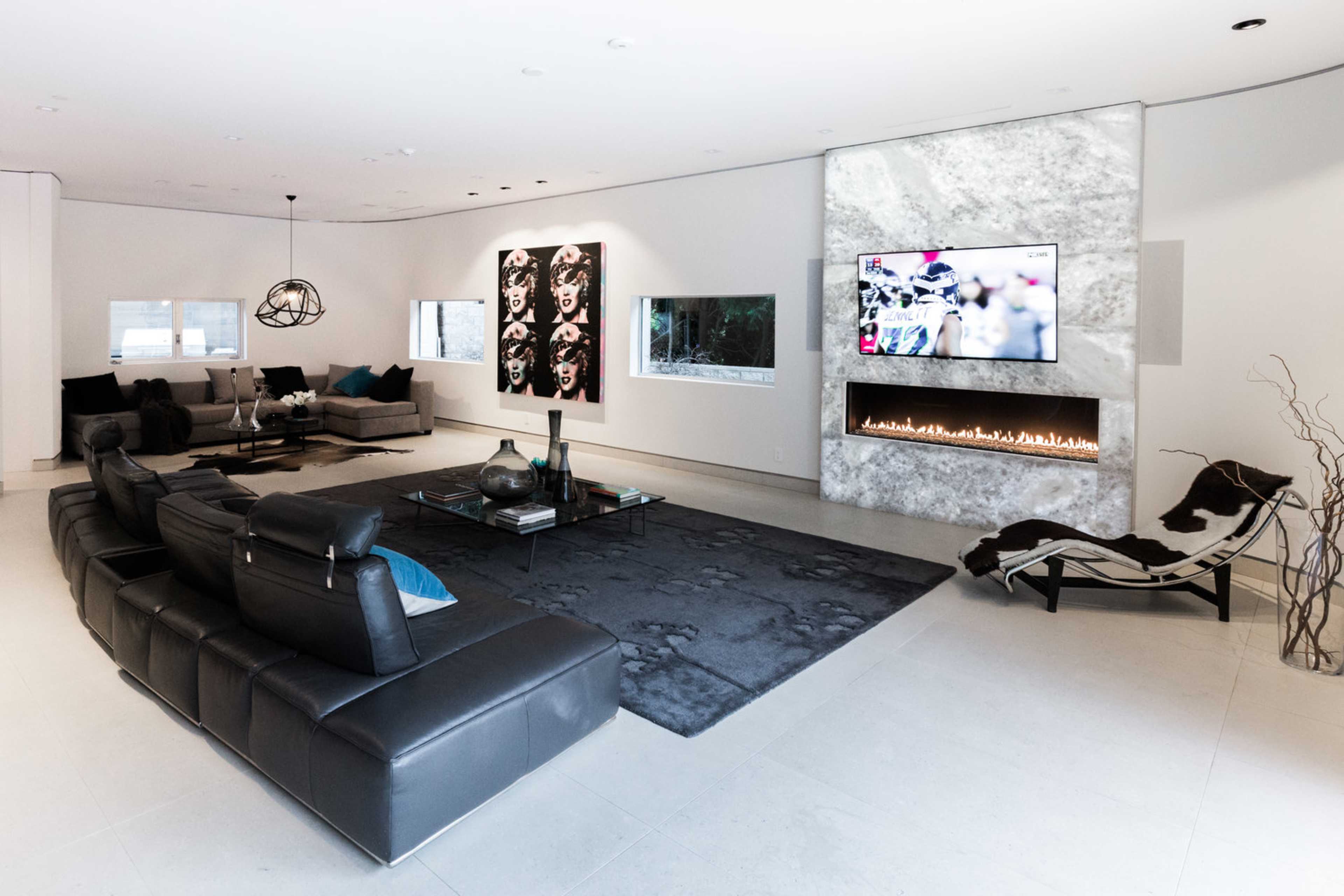 A modern living room features a sleek black sectional sofa, a flat-screen TV mounted on a stone wall, and two large artworks.