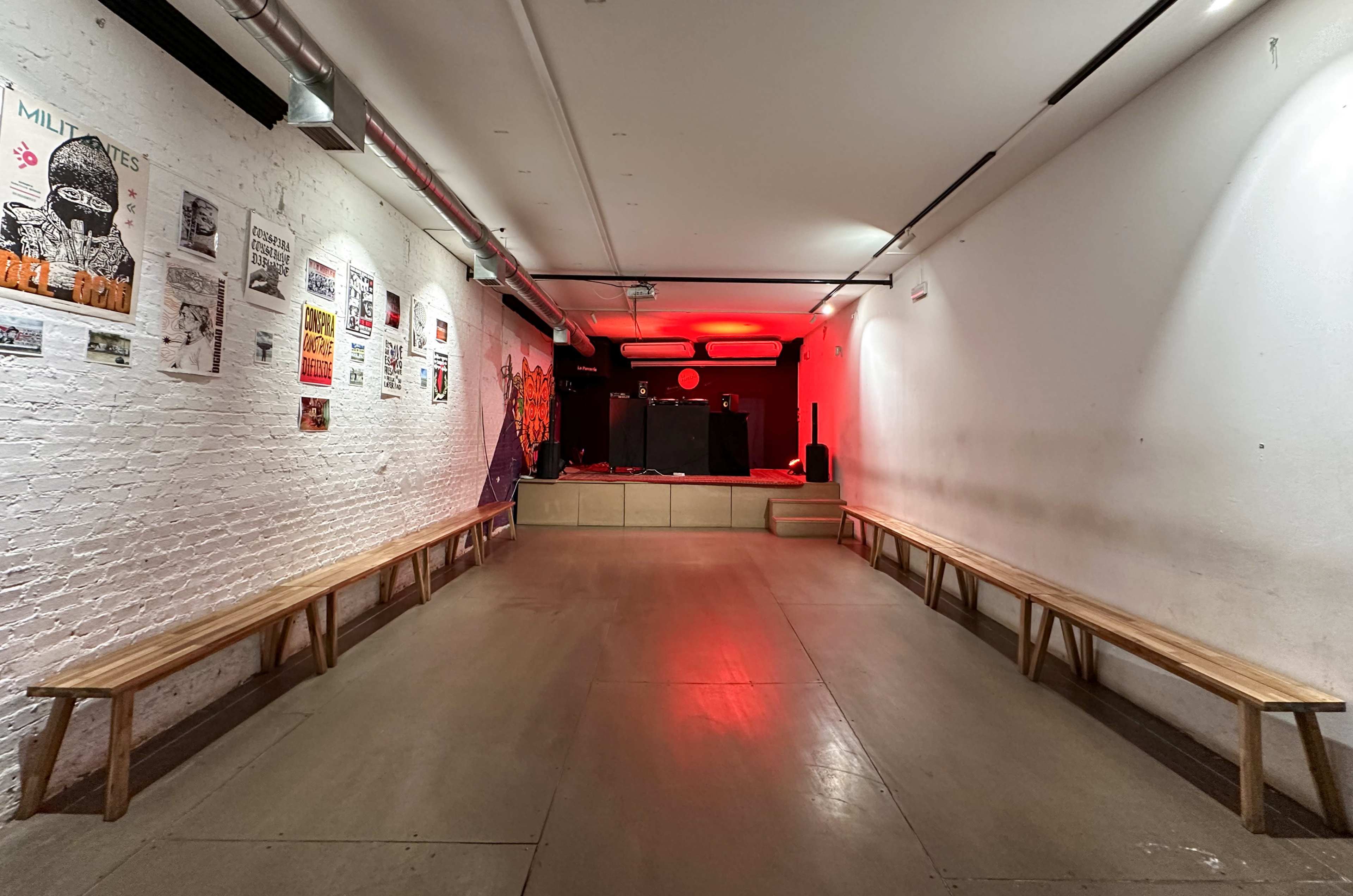 The image shows a narrow performance space with wooden benches on either side and a small stage lit with red lighting at the far end.