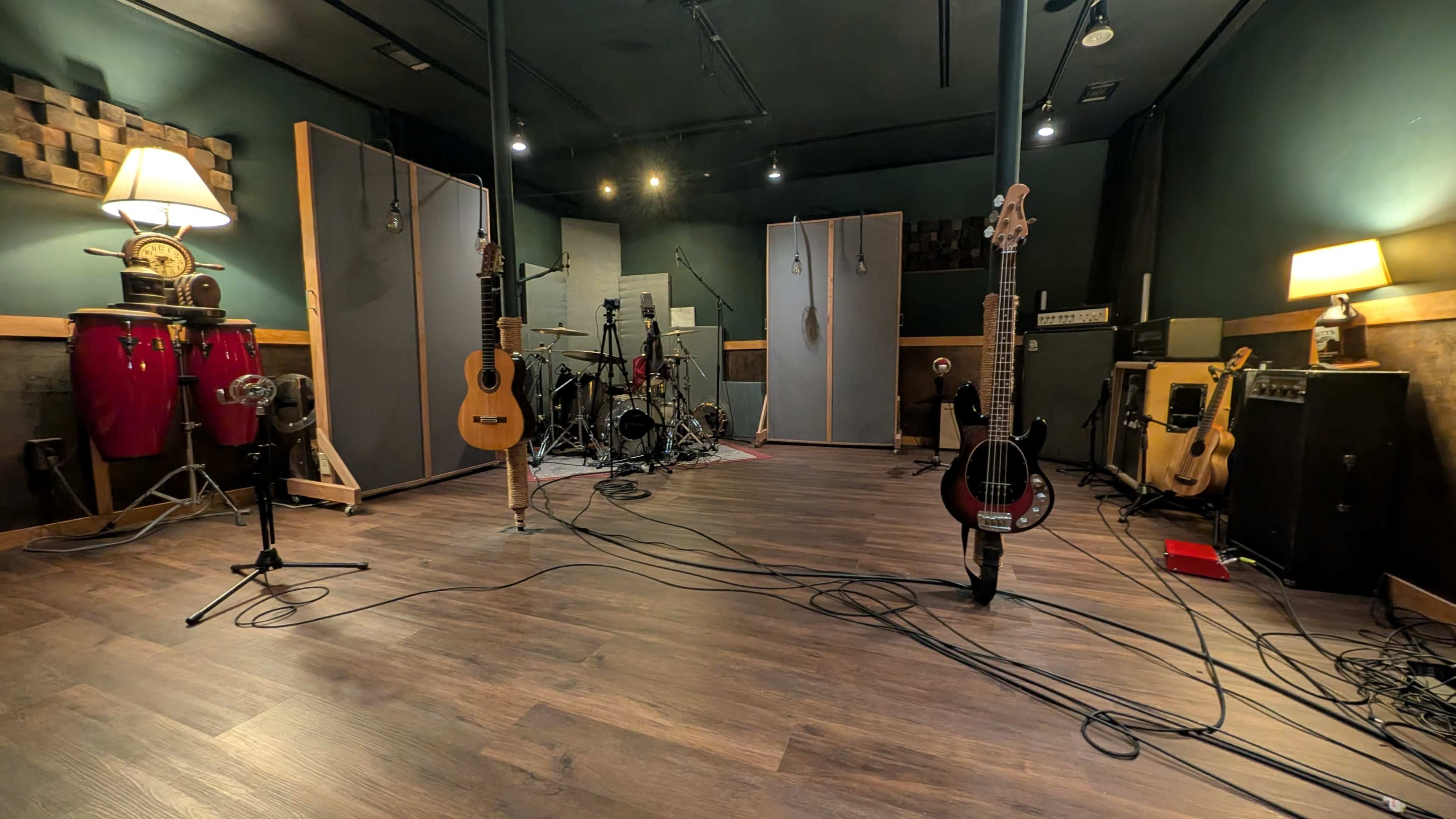 The image shows a music studio with various instruments, including guitars and percussion, arranged around a central drum set and sound equipment.