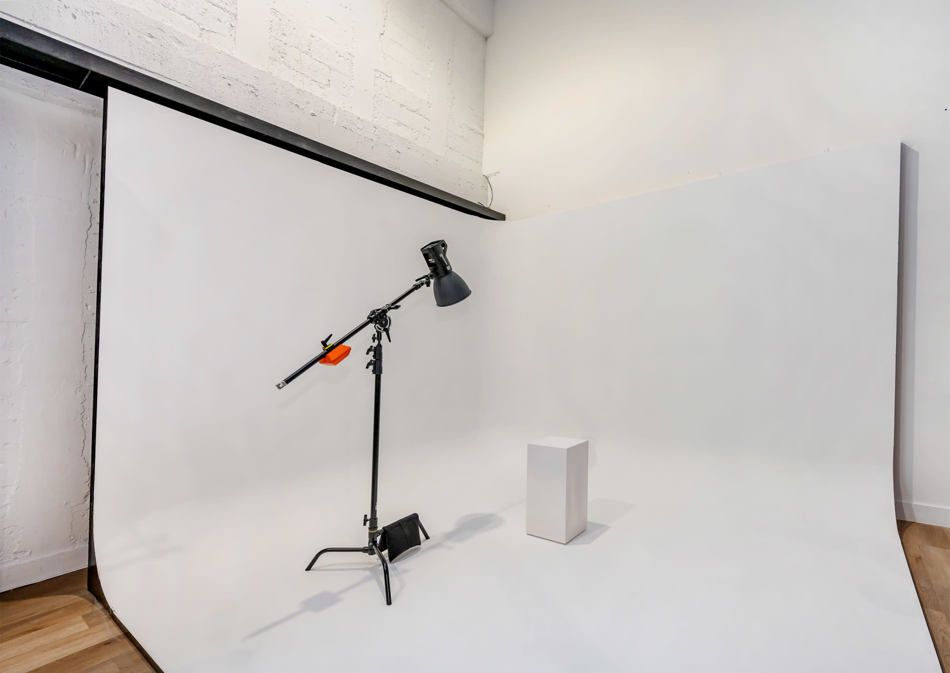 A studio space features a white backdrop with a lamp on a stand and a single white pedestal.