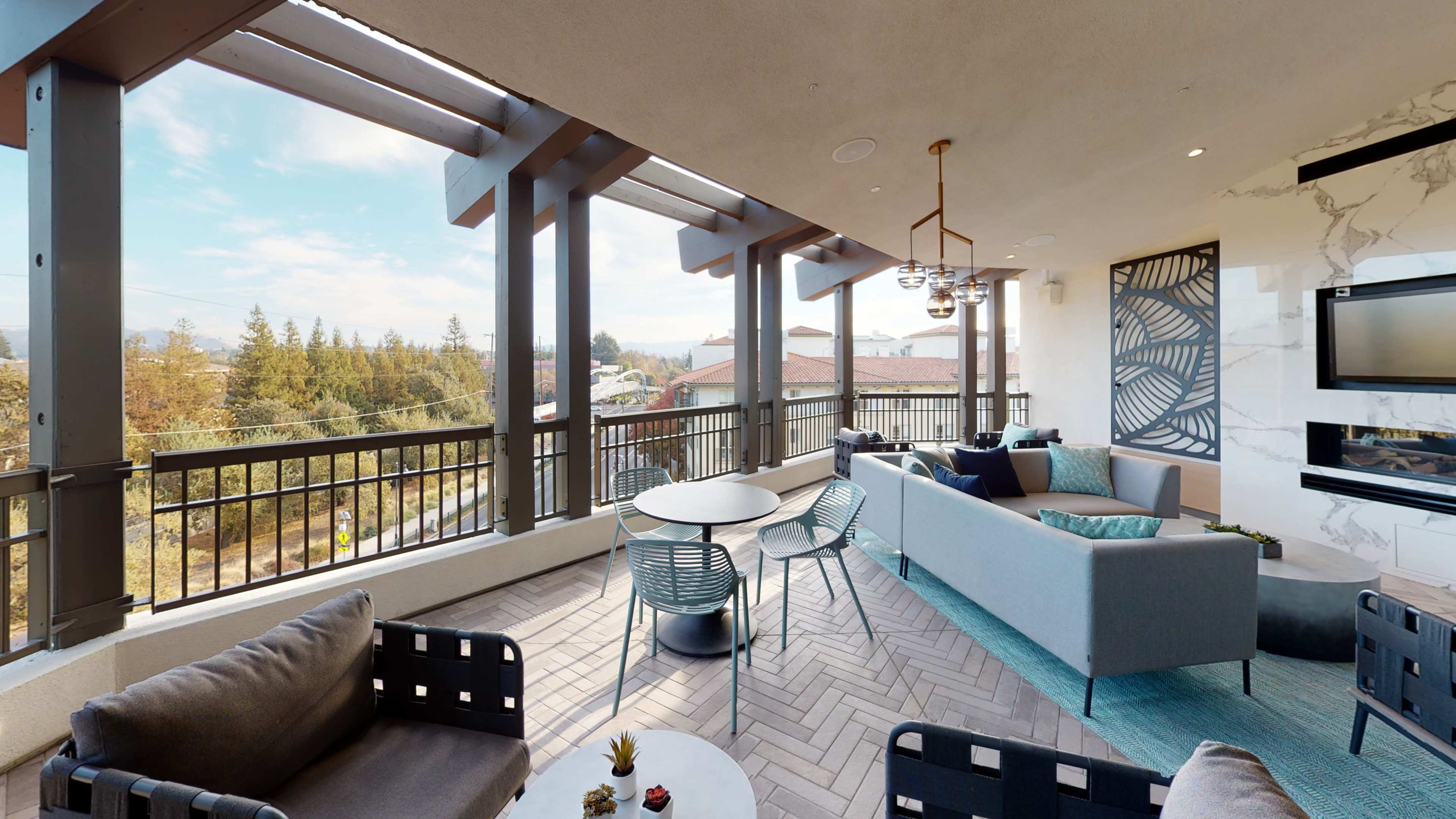 The image shows a modern balcony with a seating area that includes a couch and chairs, and a view of trees and buildings in the distance.