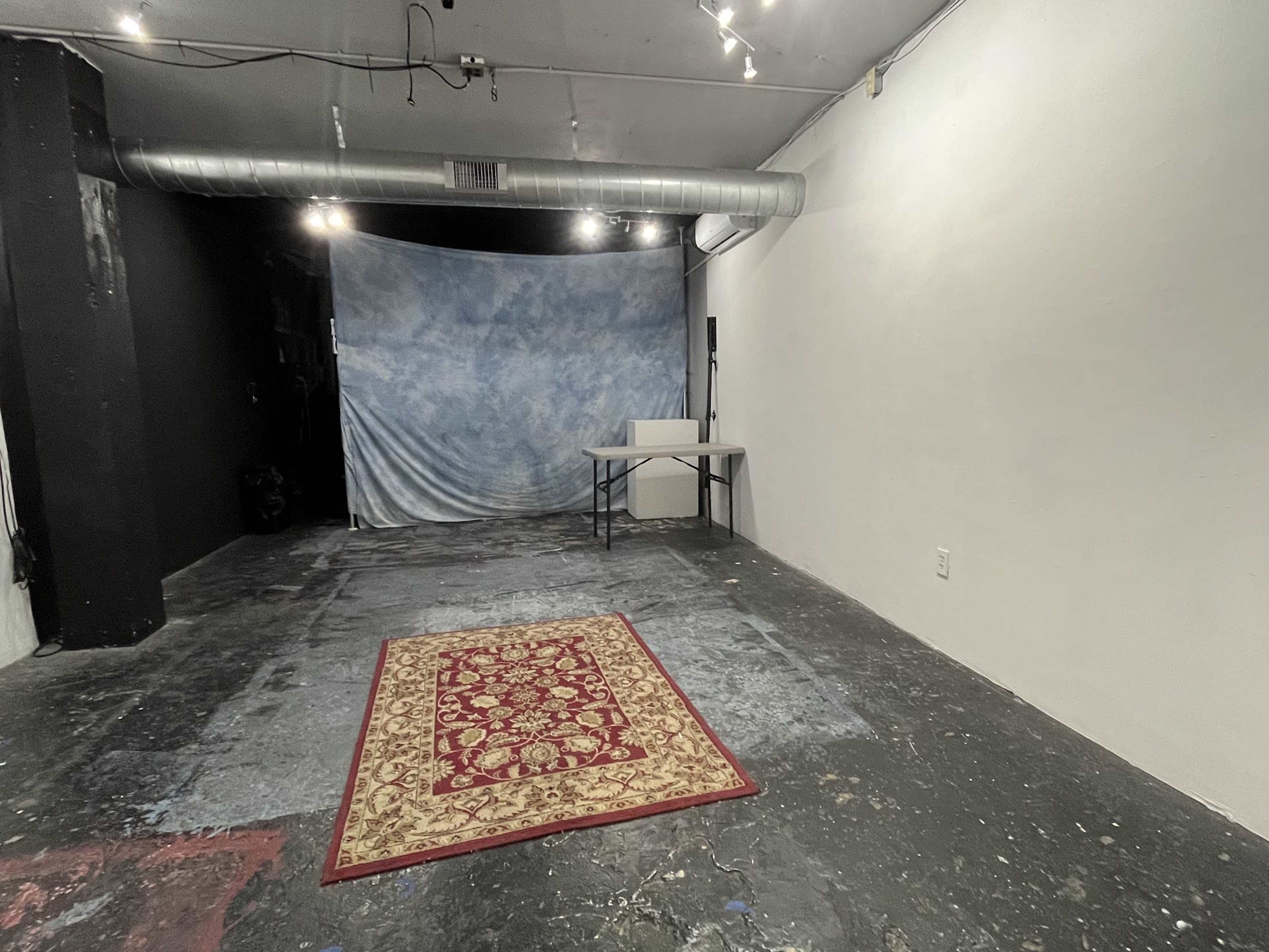 The image shows a sparse room with a dark floor, a blue backdrop draped against the wall, and a small table placed in the center.